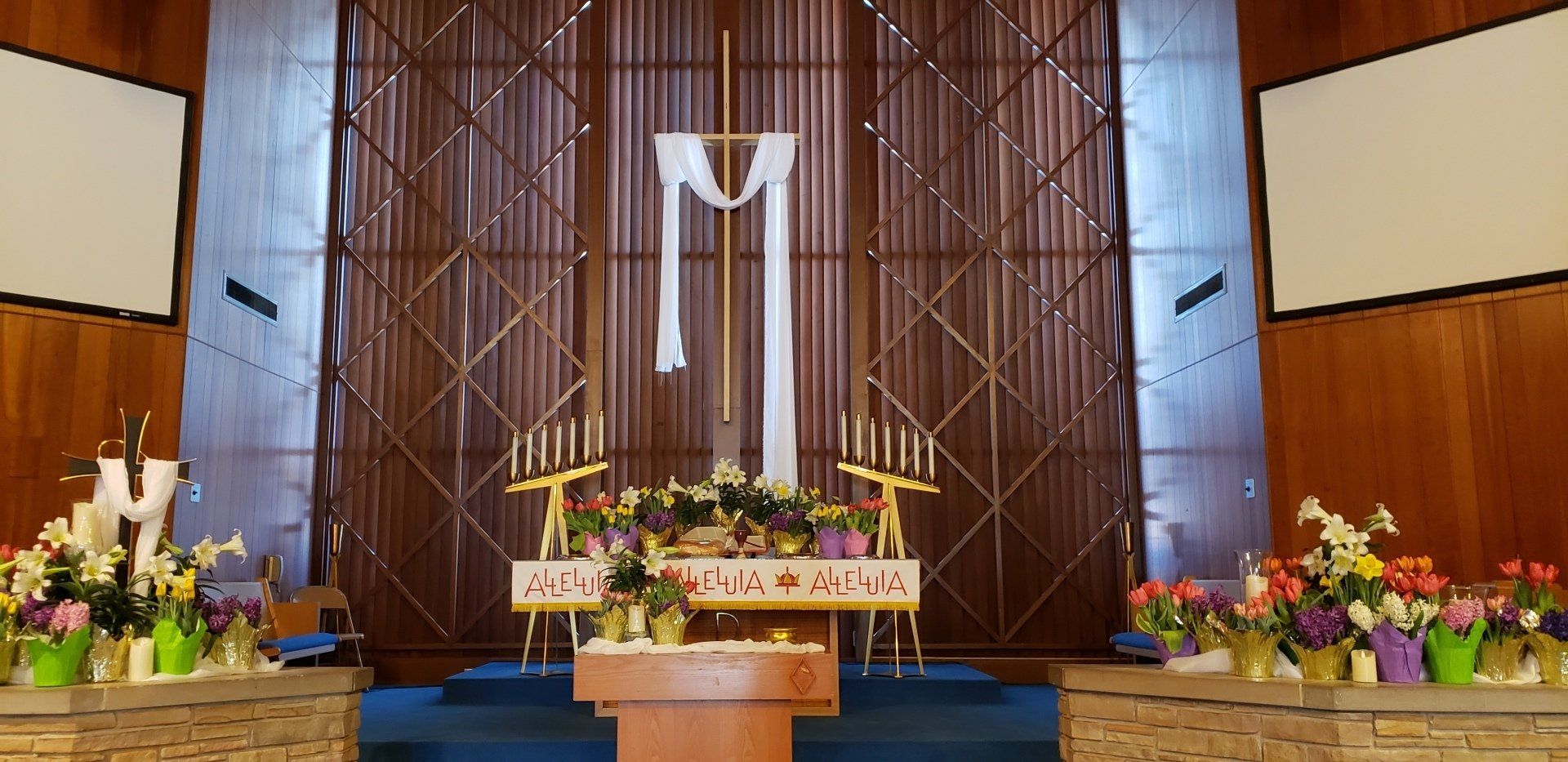 Church altar with a large white cross banner, flowers, and a central lectern on a blue carpeted stage