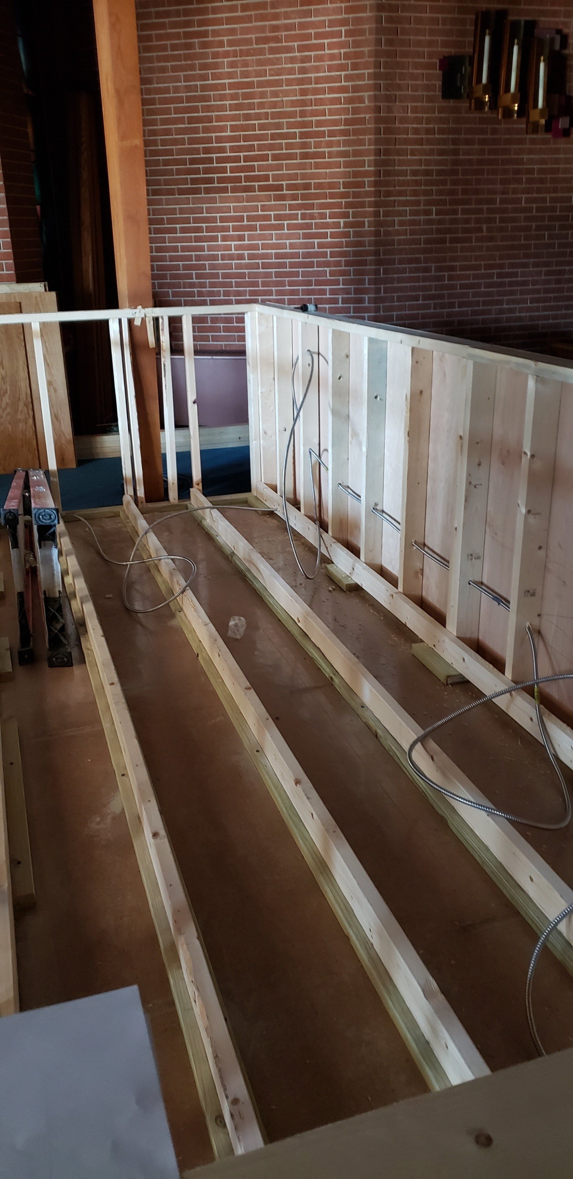 Partially framed room with exposed floor joists and white wall studs against a brick wall