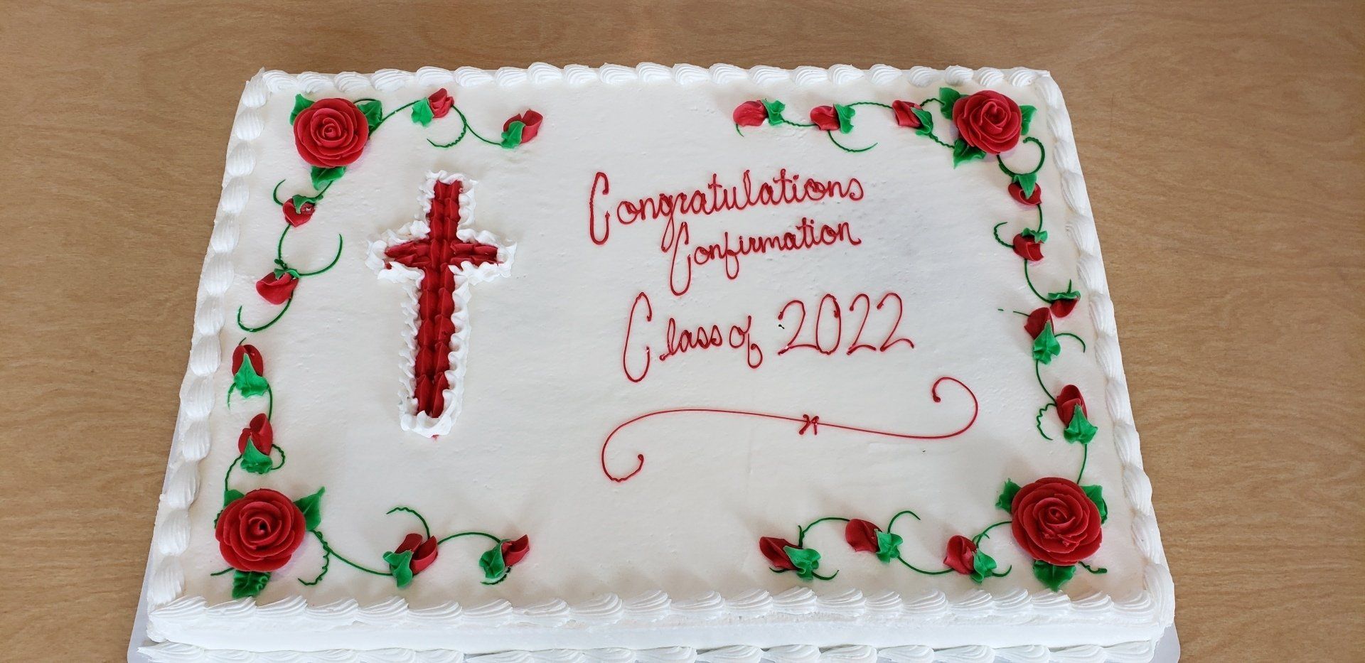 White decorated cake with red cross and red-green floral icing, reading “Congratulations on your Confirmation 2022.”