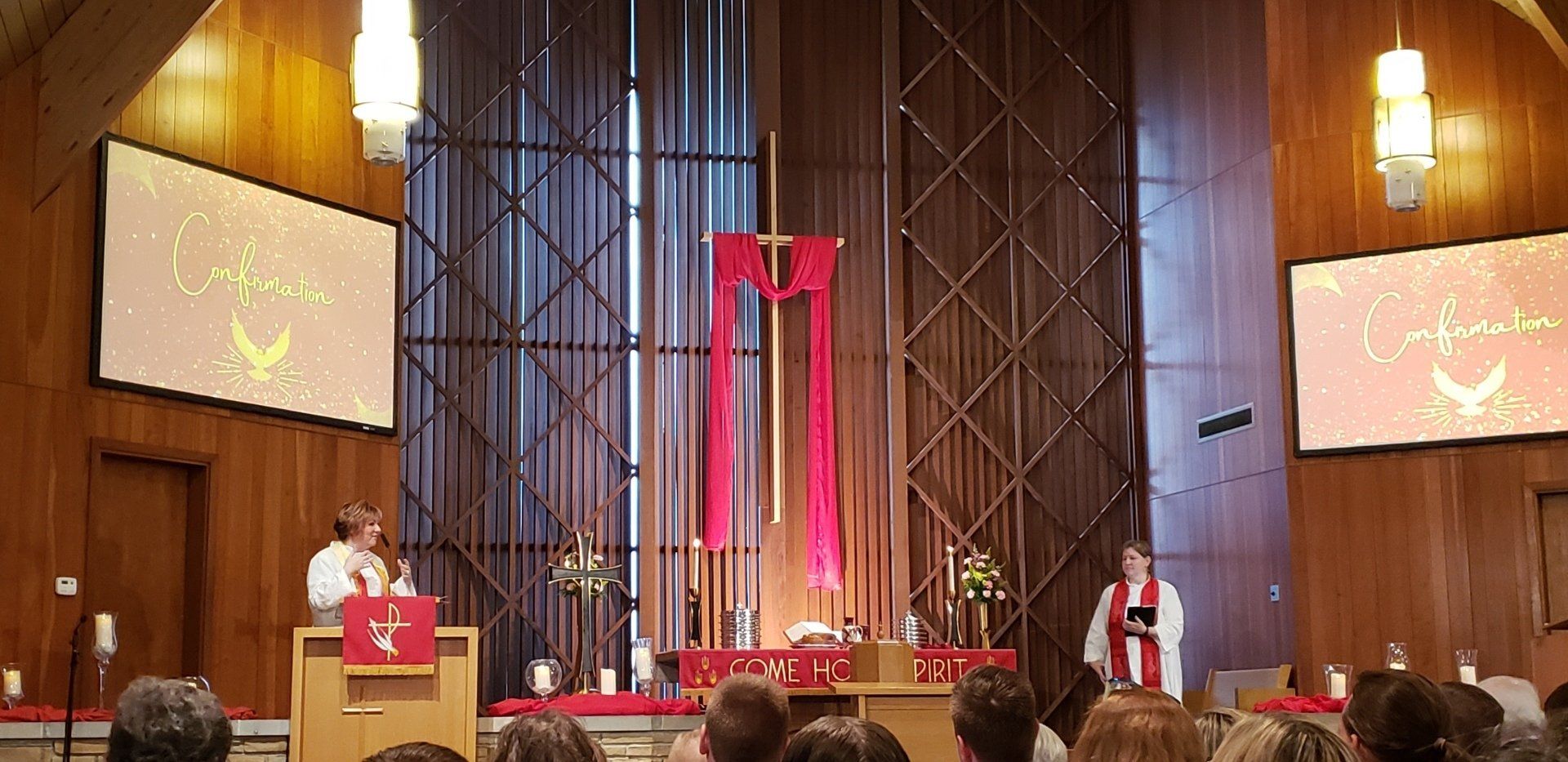 Church sanctuary with a red-draped cross on stage, podium speaker, and projected screen presentation