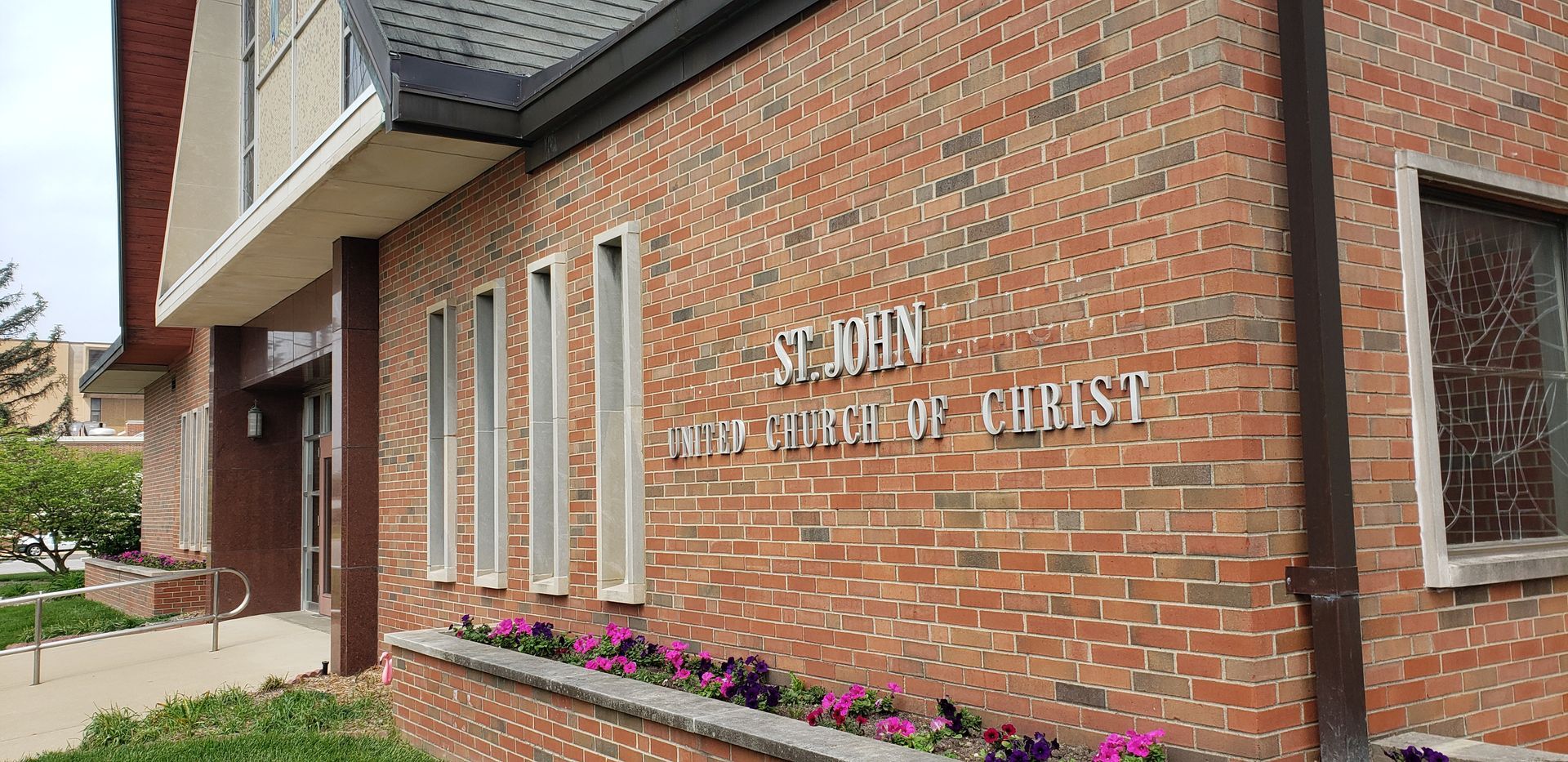 Brick church wall with white lettering and flower bed along the sidewalk