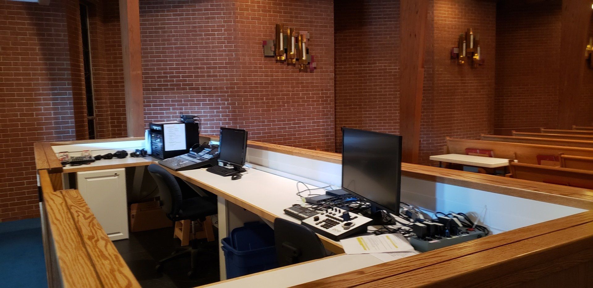 Empty office control room with desks, monitors, and audio equipment against brick walls.