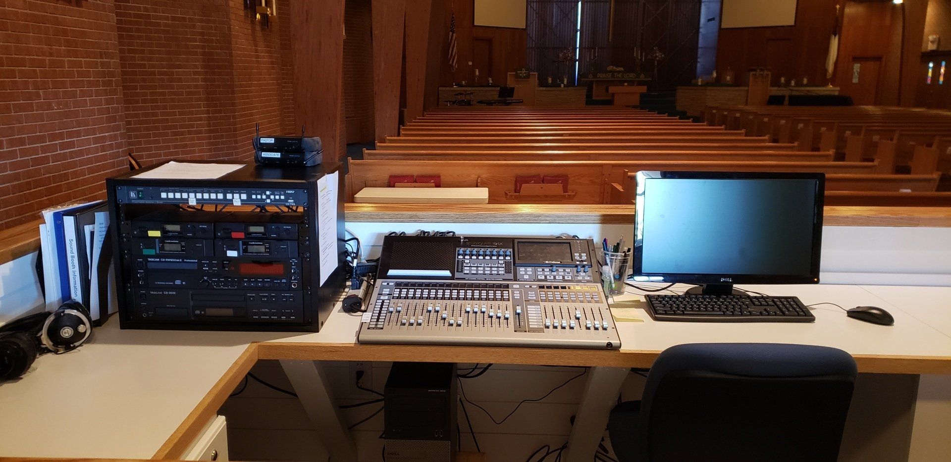 Church sound booth with audio mixer, laptop, monitor, and keyboard facing the sanctuary.