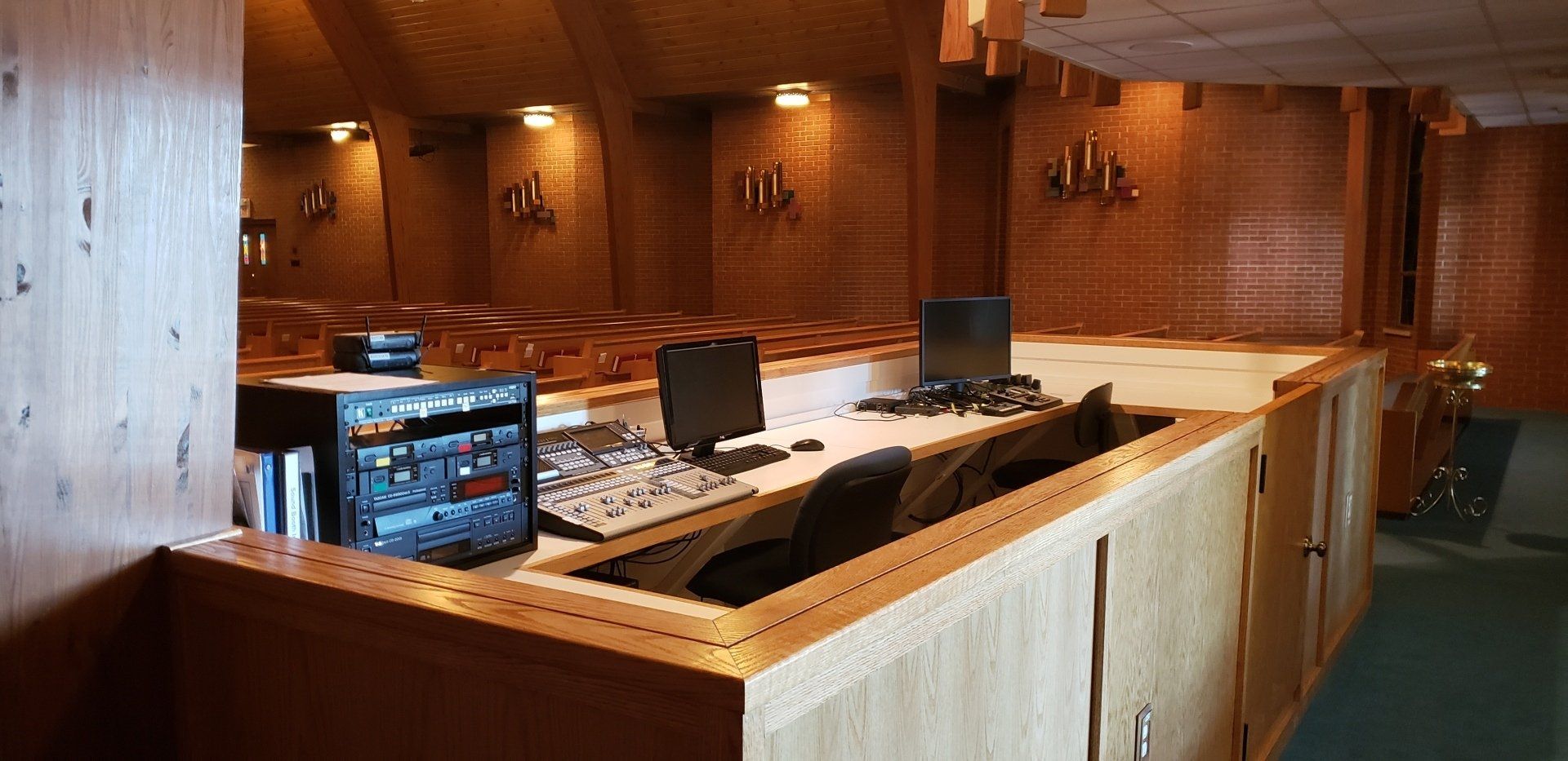Wood-paneled control room with monitors, mixing consoles, and office chairs behind a wooden barrier
