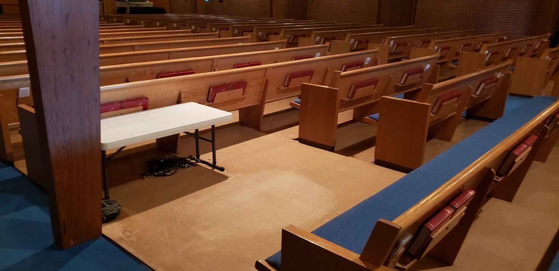 Empty church sanctuary with wooden pews, blue cushions, and a white table at the front