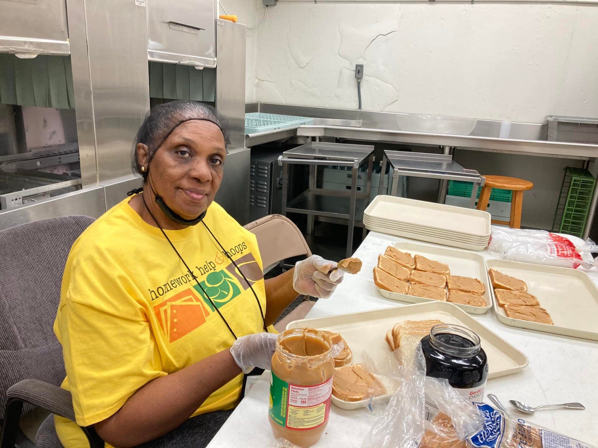 Person in yellow shirt packaging sandwiches in a kitchen prep area.