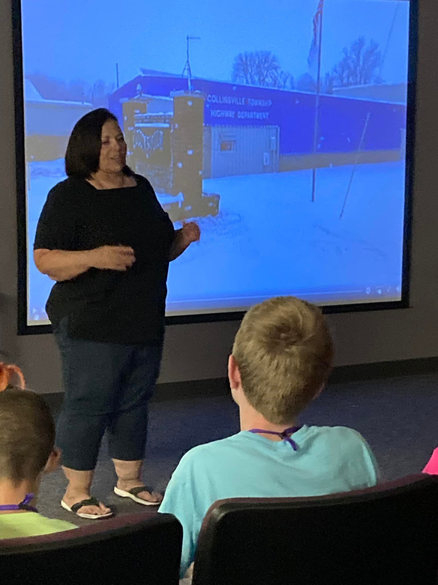 Presenter speaking in front of a projected slide while seated students watch in a classroom