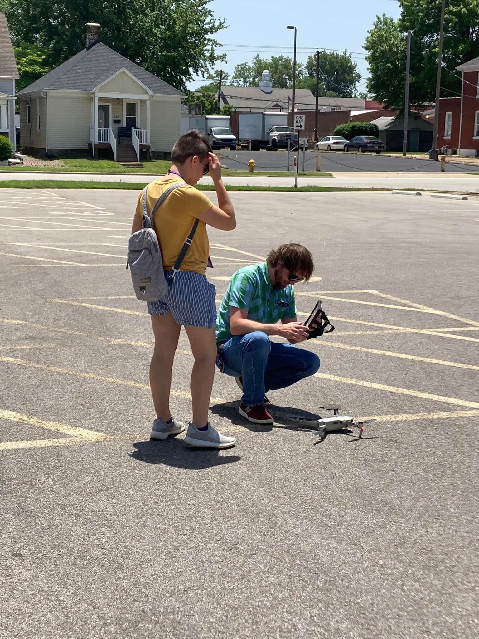 Two people crouch and stand on a sunny street, examining a small object on the pavement.