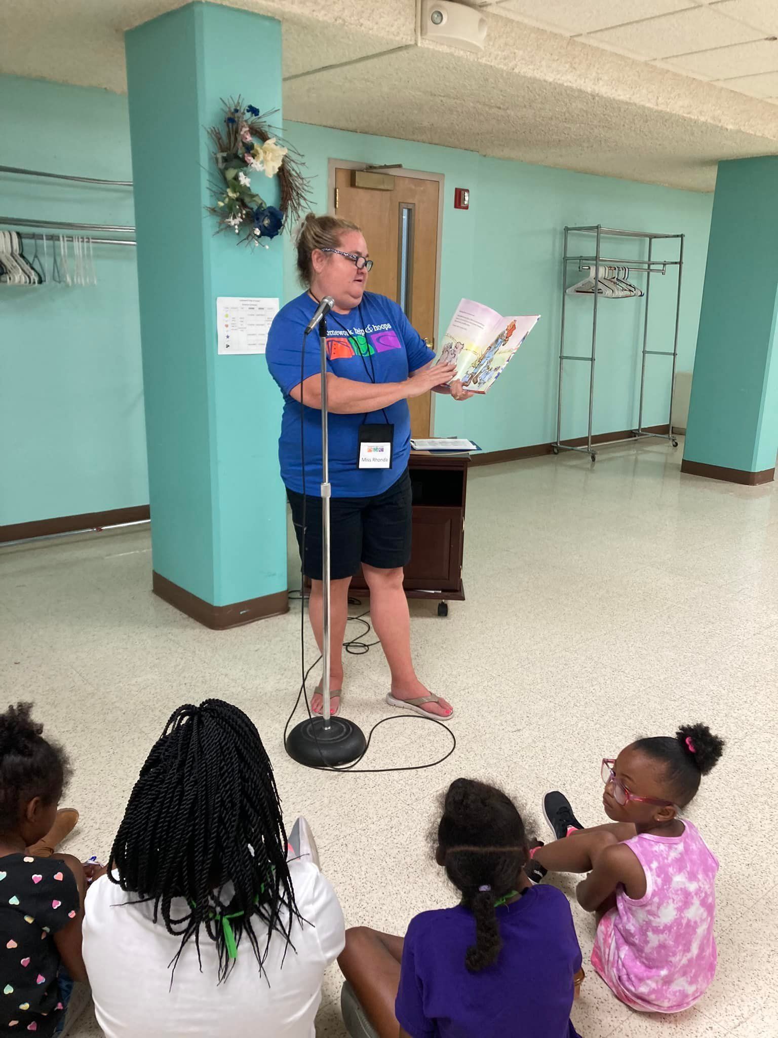 Woman reading from a book to seated children in a community room