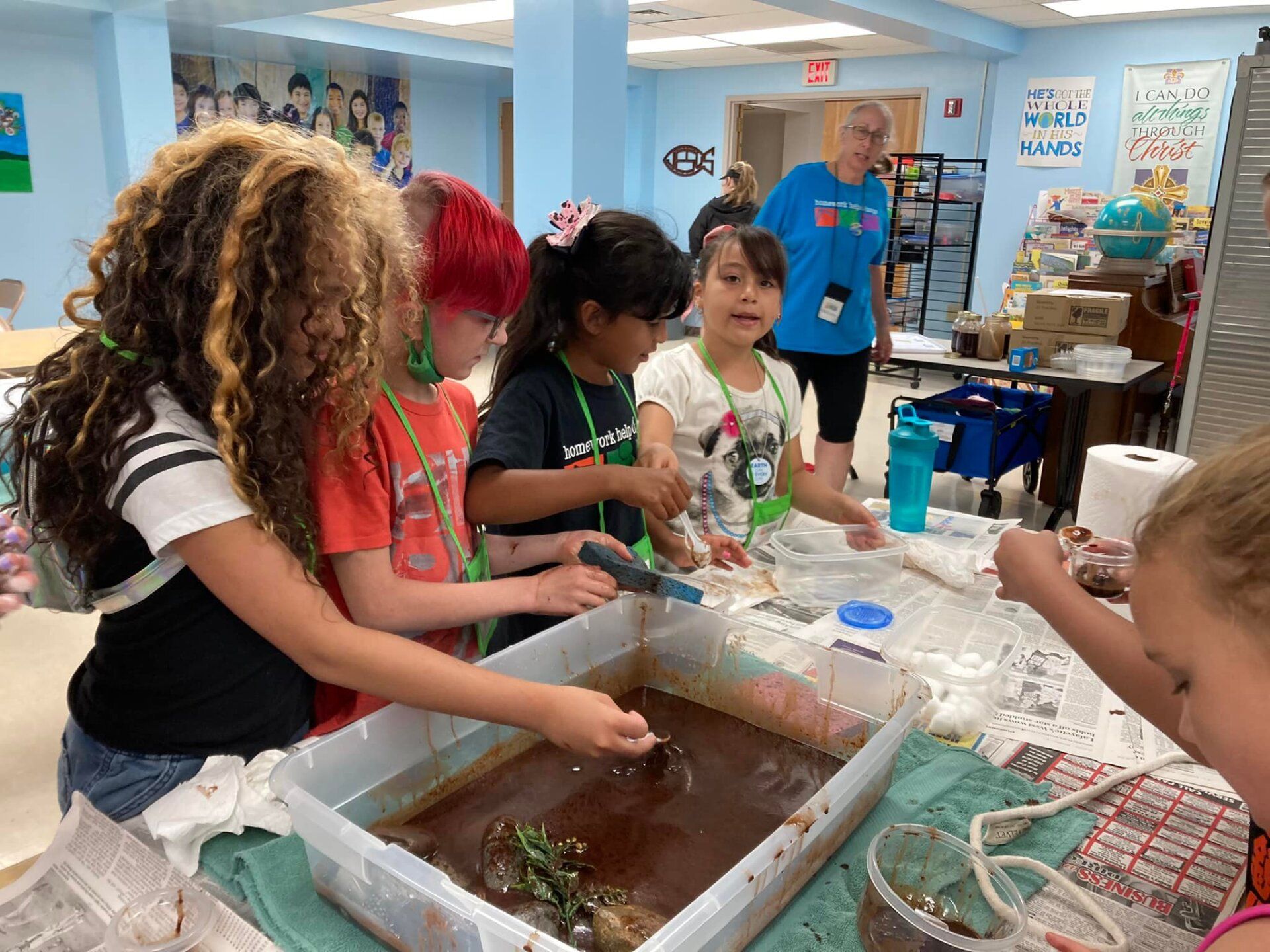 Children making a hands-on activity at a table in a classroom or workshop, with supplies and a presenter nearby