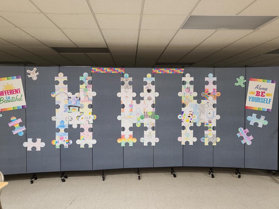 Classroom display board with colorful puzzle-piece decorations and posters on a gray wall