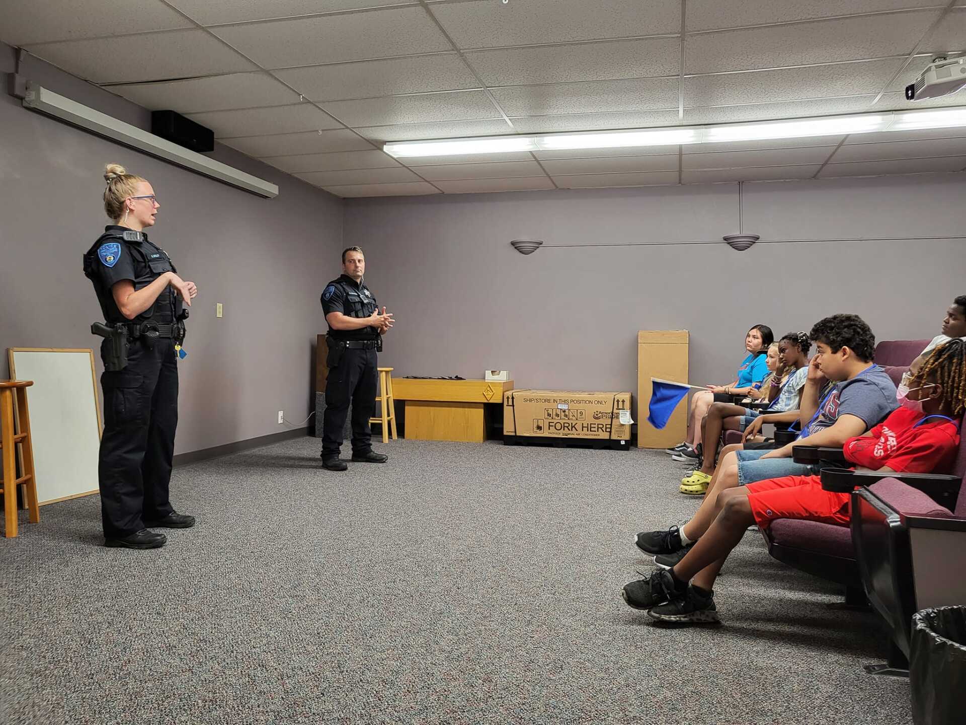 Two presenters speak to a seated audience in a conference room.