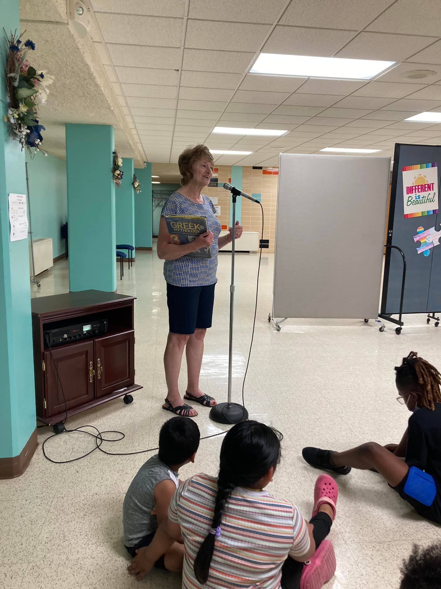 Speaker at microphone in classroom with children seated on the floor listening