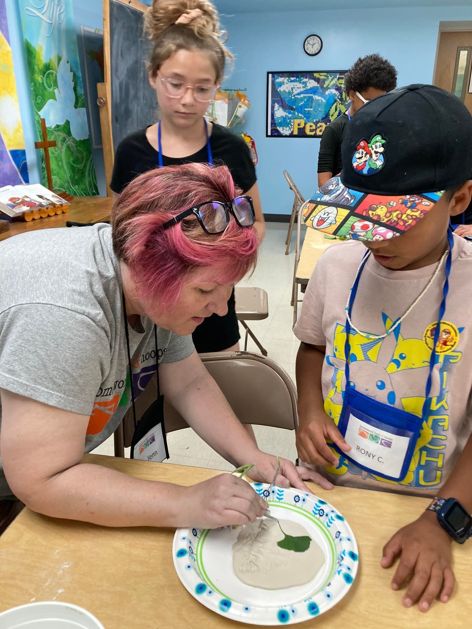 Teacher guiding two children in a classroom art activity around a paper plate project