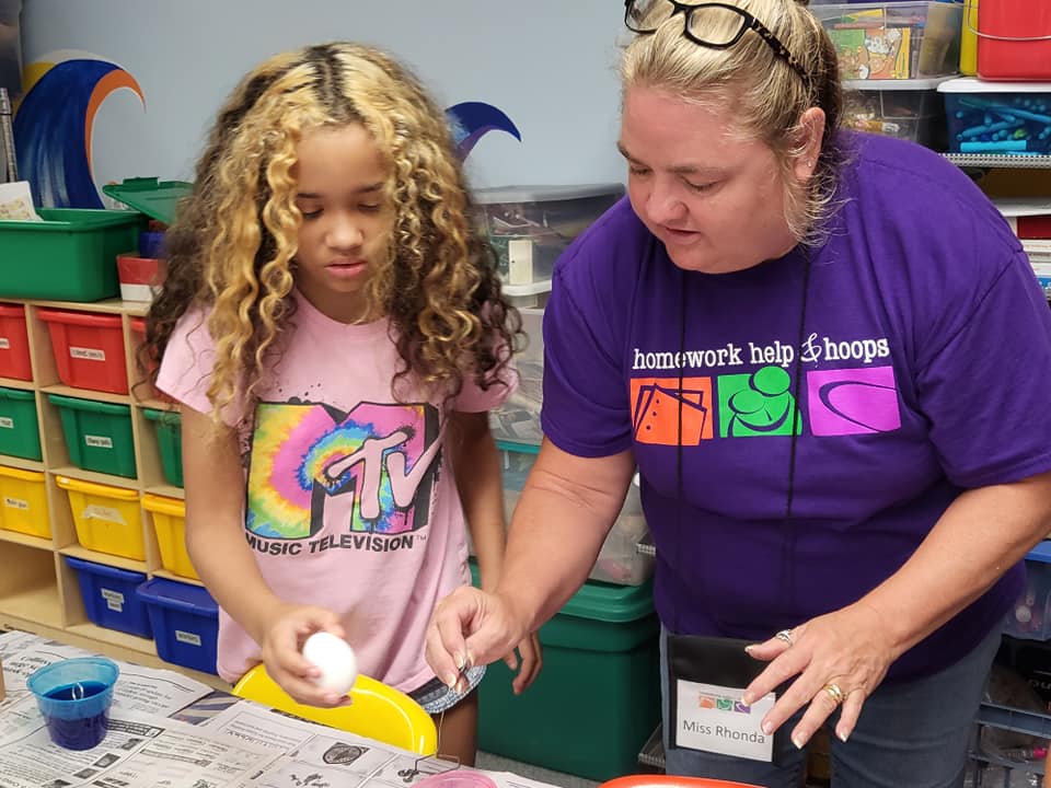 Adult and child using a paint roller at a table in a colorful classroom