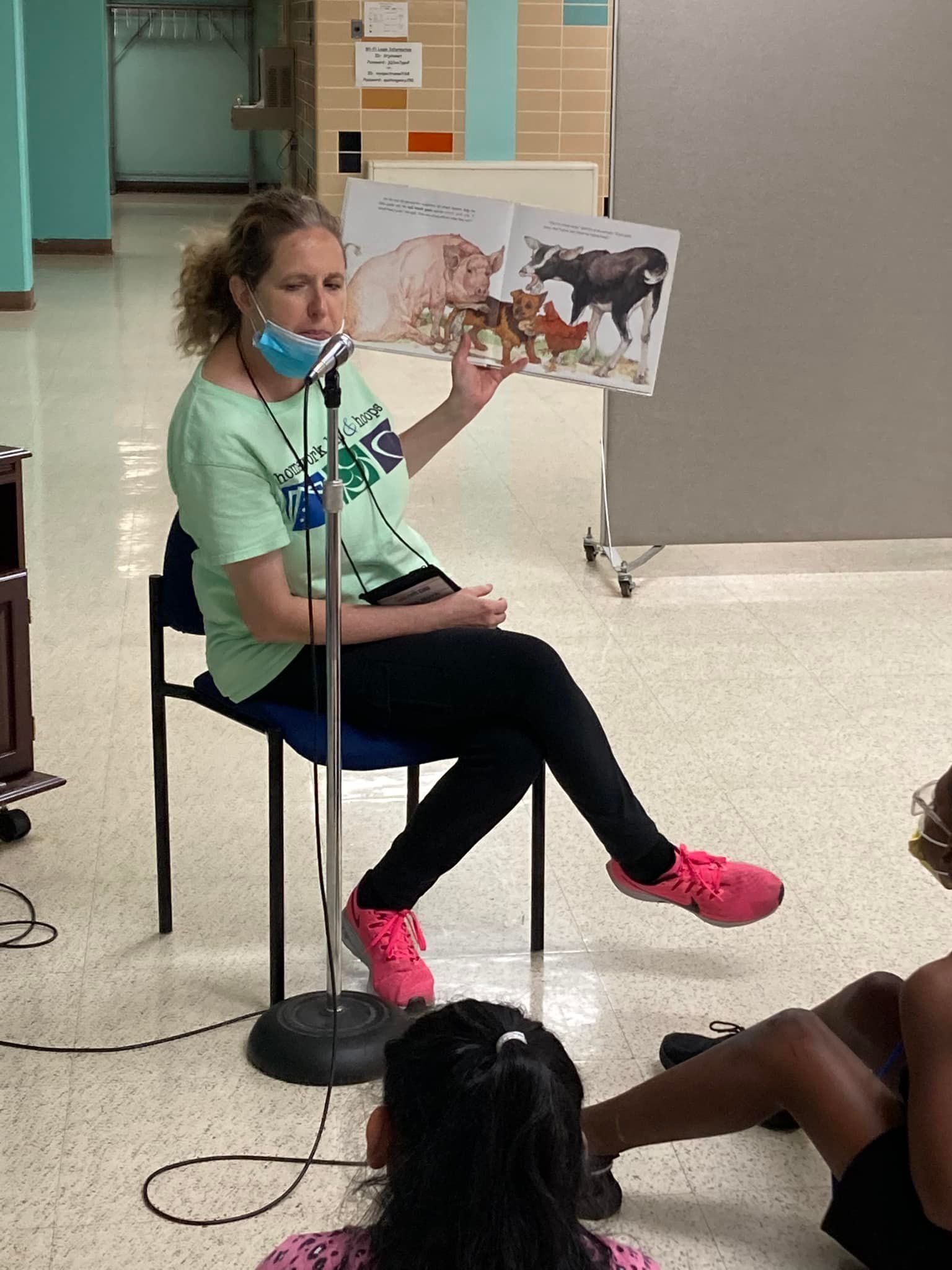Woman seated on a chair reads from a book to children in a classroom setting.