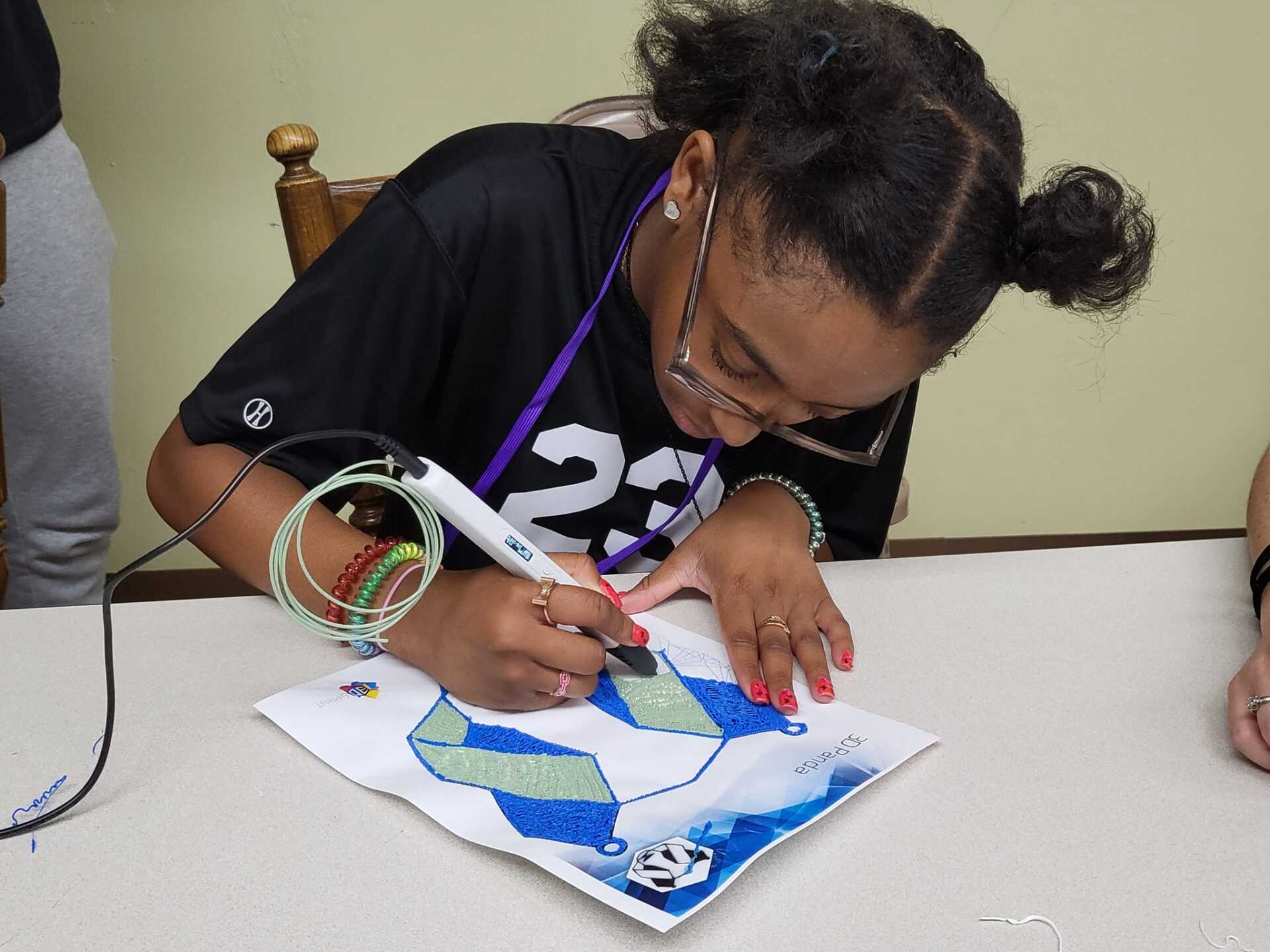 Person seated at a table, painting a blue-and-green paper craft with a marker.