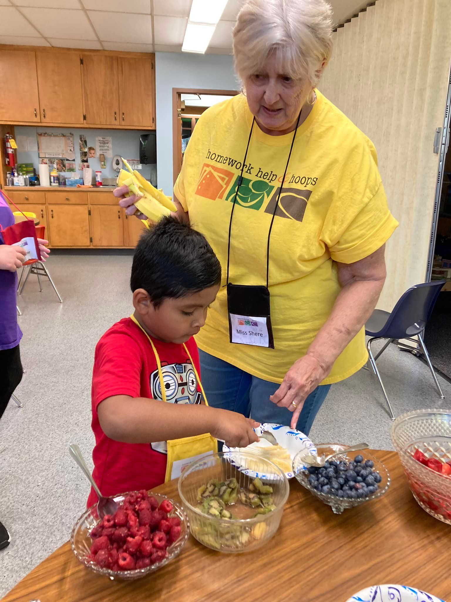 Woman and child making a fruit snack at a table with bowls of strawberries, blueberries, and bananas