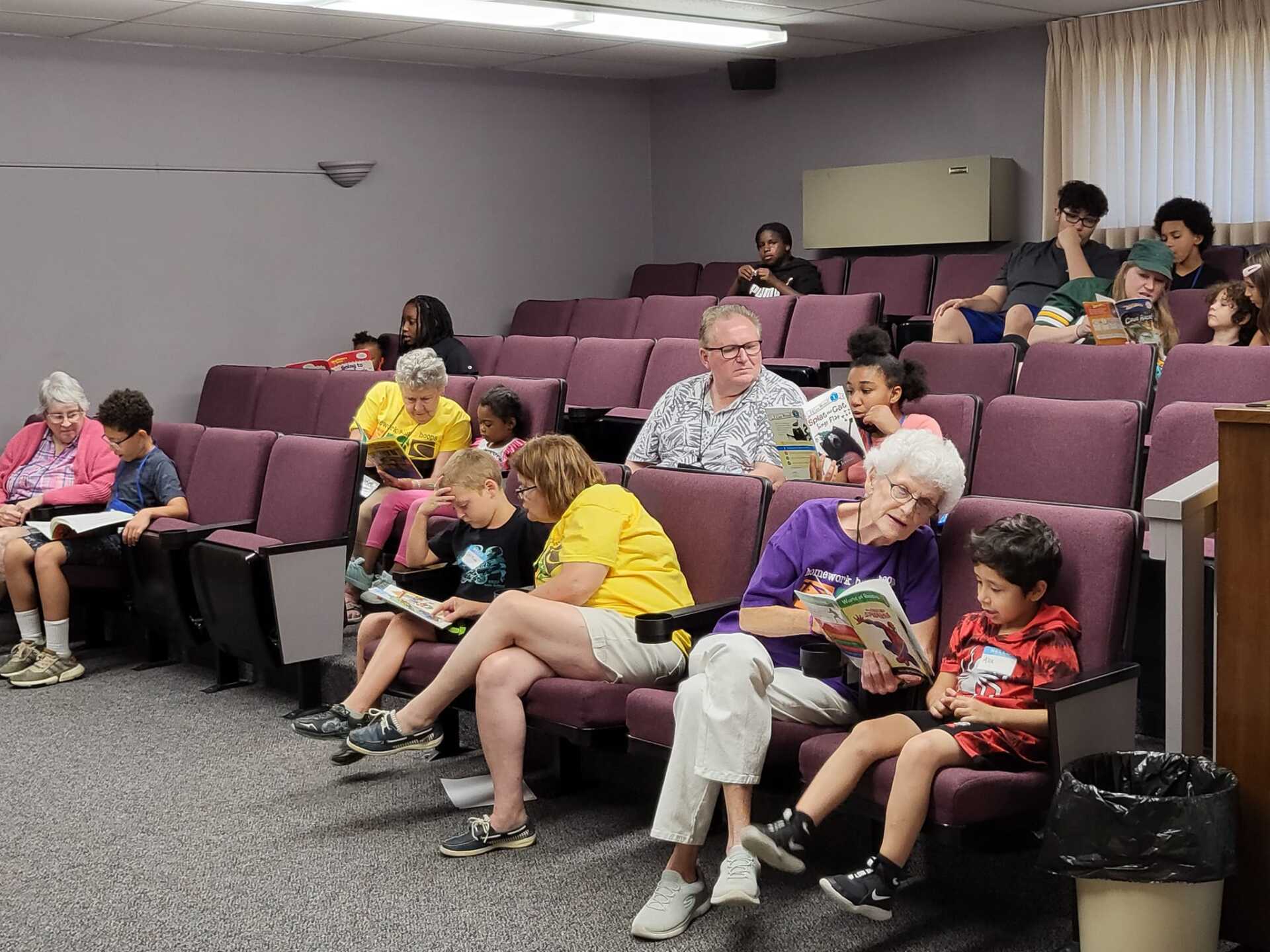 People seated in a lecture hall-style room, some chatting and reading papers.