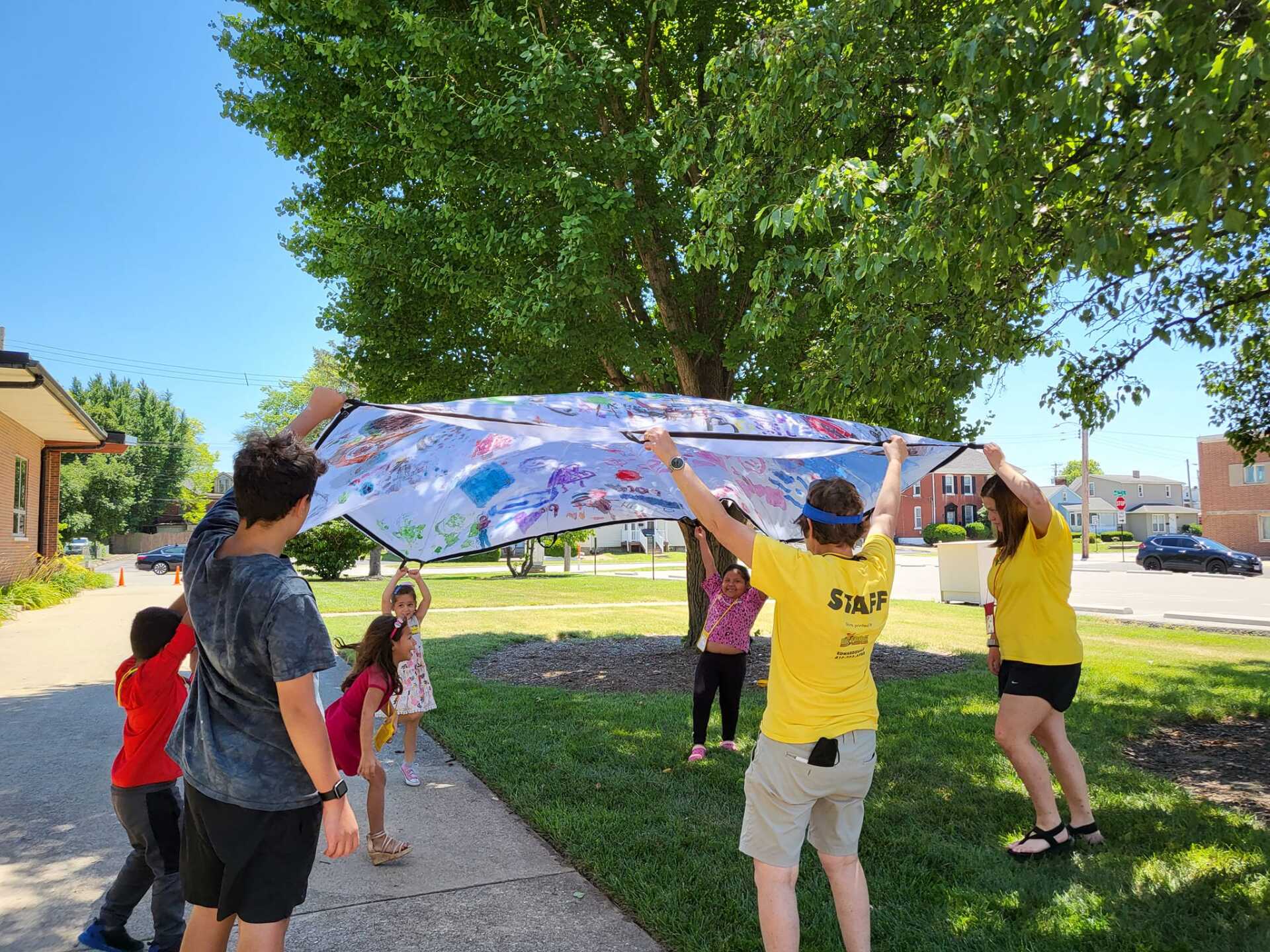 People holding a colorful parachute outdoors under a tree at a park