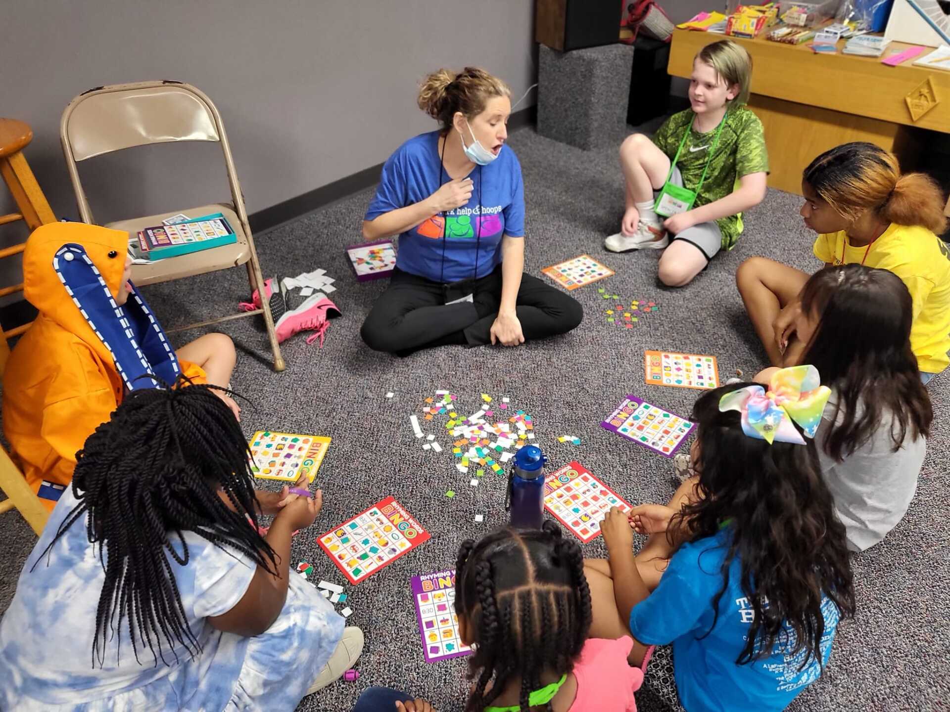 Children sitting in a circle on a carpet, playing a board game with colorful pieces and cards