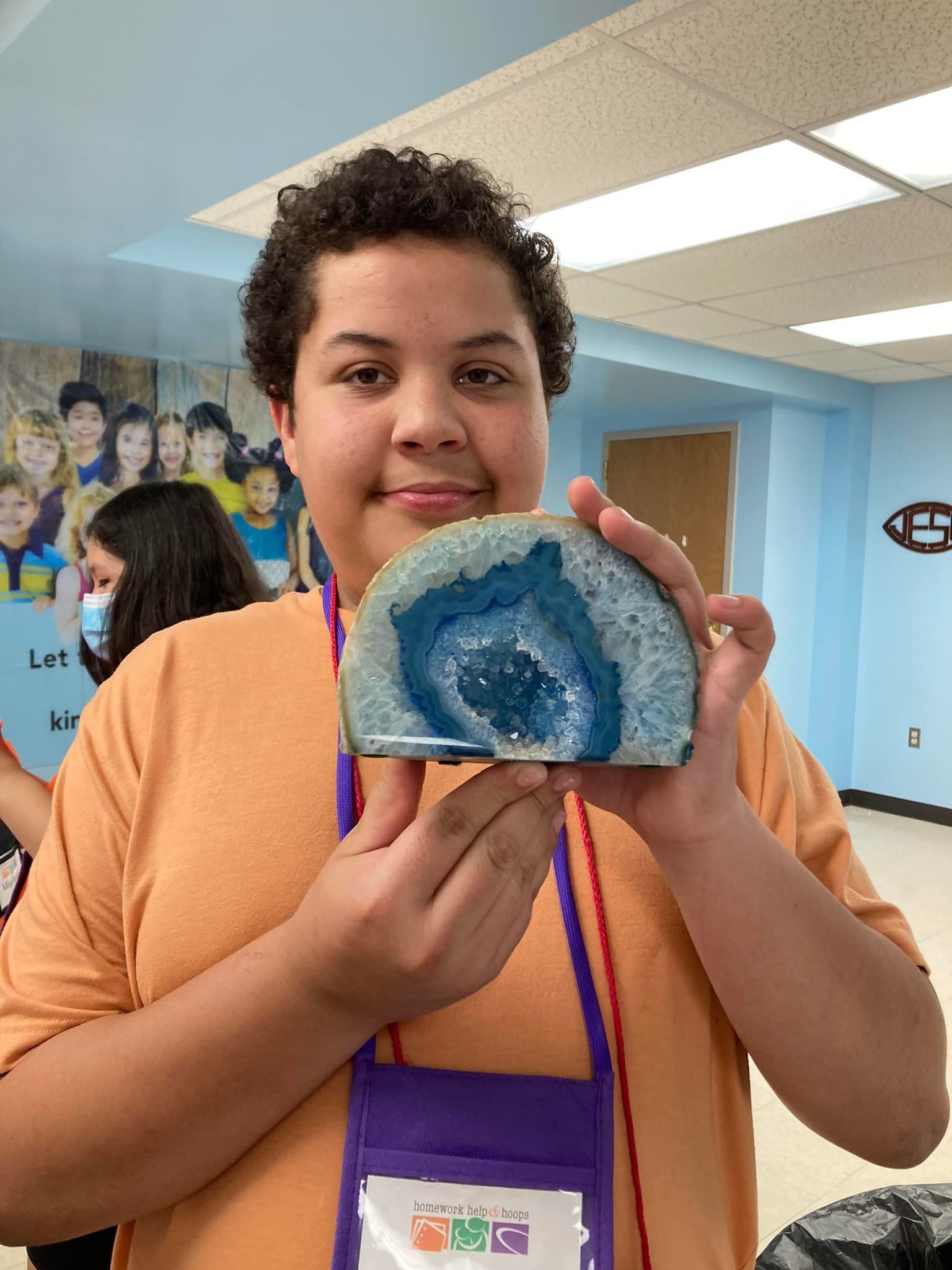 Person in a classroom holding up a blue geode slice and smiling at the camera.