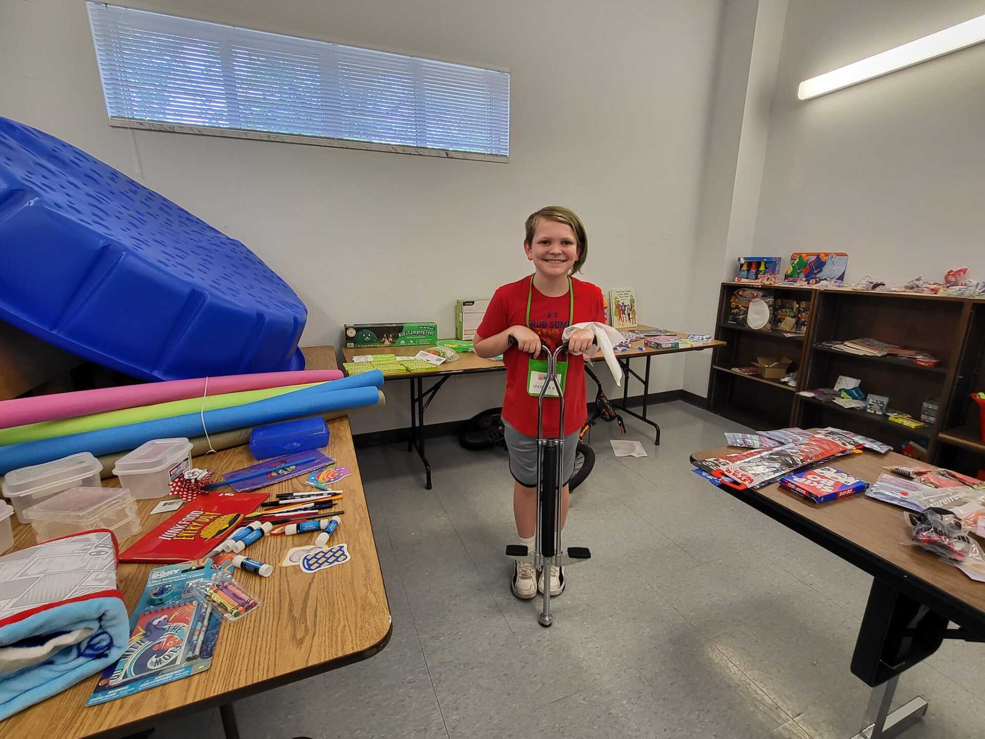 Person on a scooter in a room with tables covered in colorful snacks and toys, smiling at the camera
