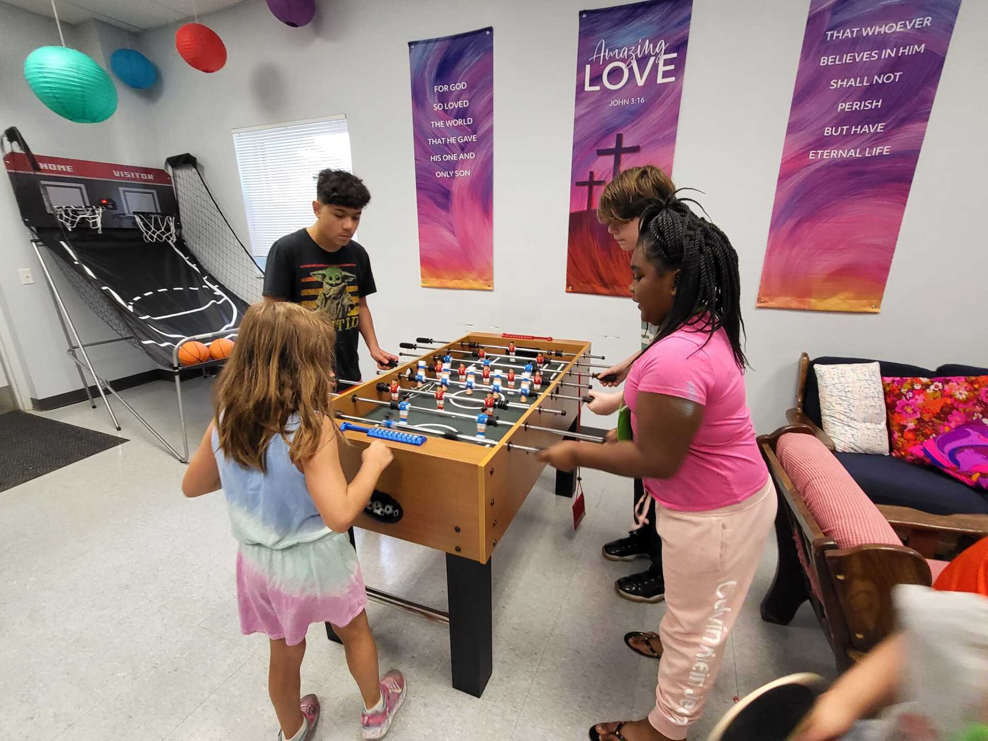 People playing foosball in a colorful room with wall banners and a couch.