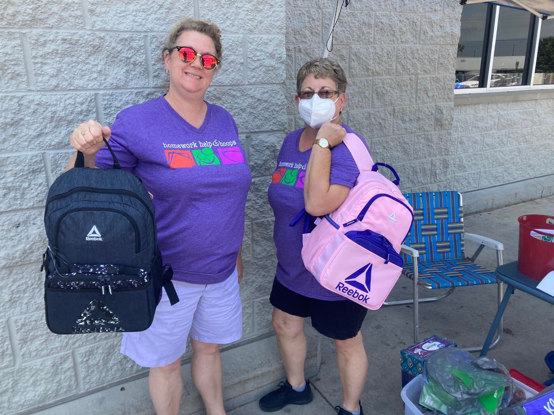 Two people in purple shirts holding backpacks outside a building.