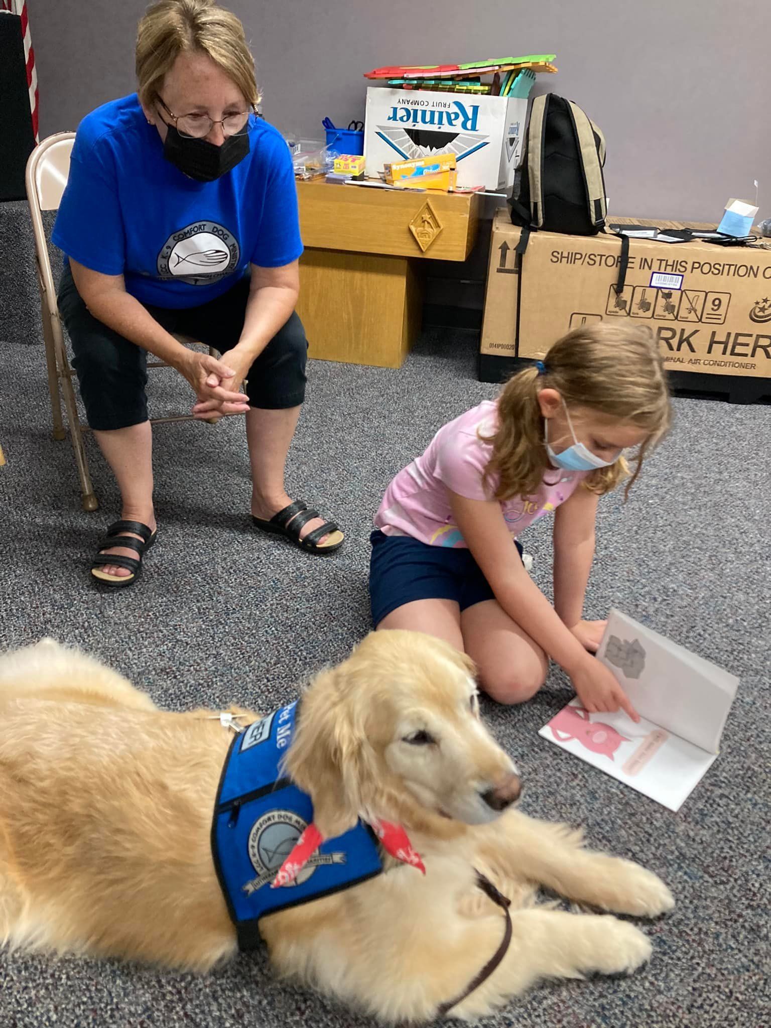 Woman and girl pet a golden retriever therapy dog indoors.