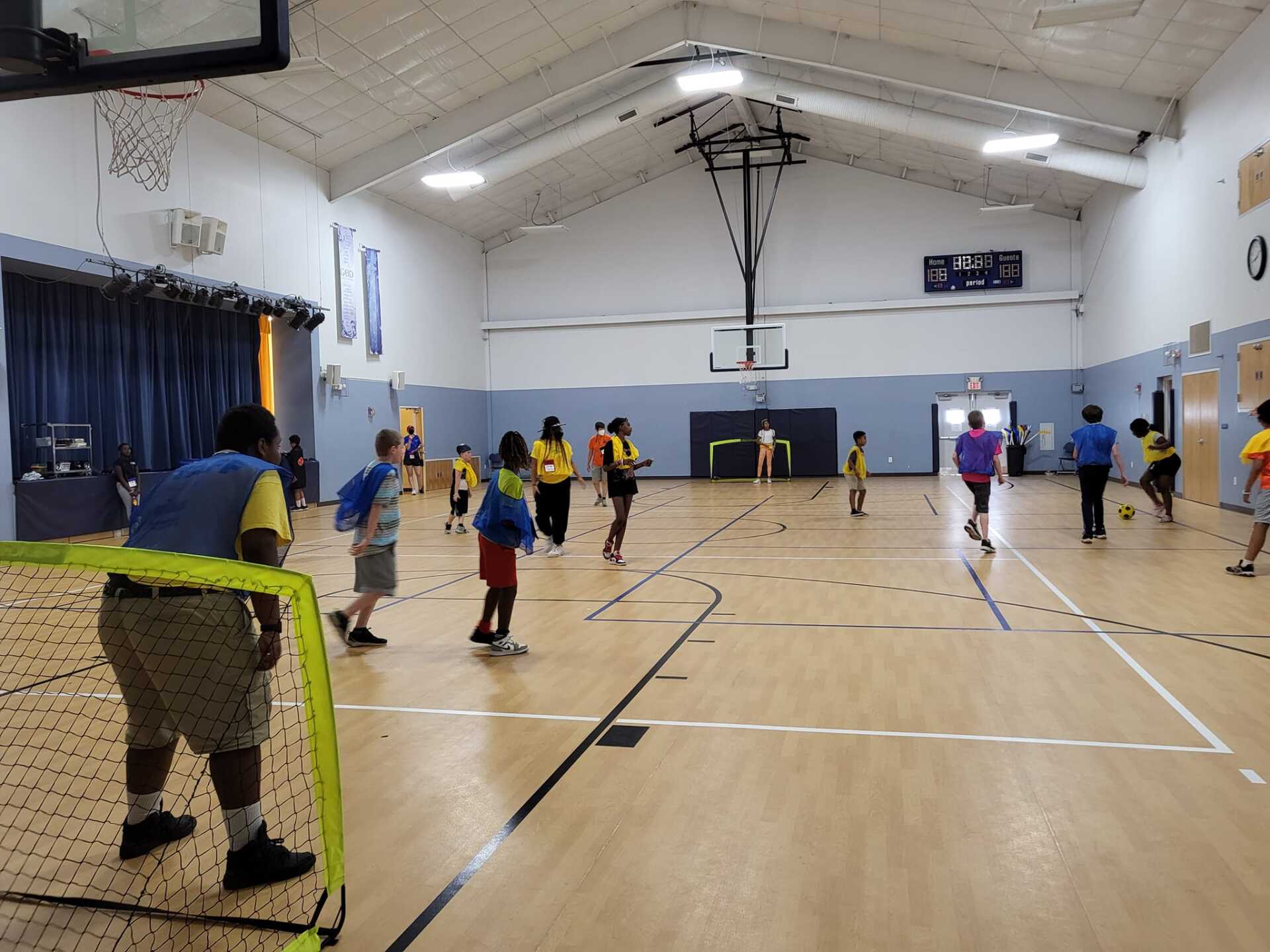 People playing indoor volleyball in a gym, with a yellow net and wooden court.