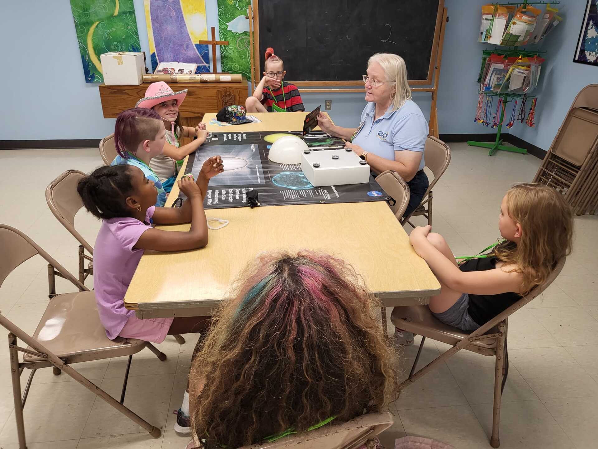 Children playing a board game at a classroom table with a teacher supervising