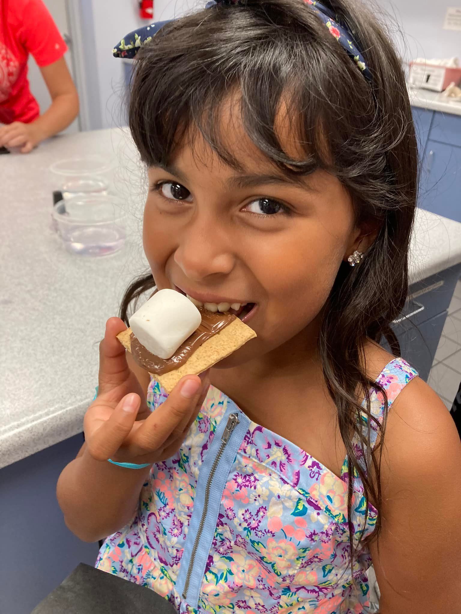 Child smiling while holding a s'more in a bright indoor setting
