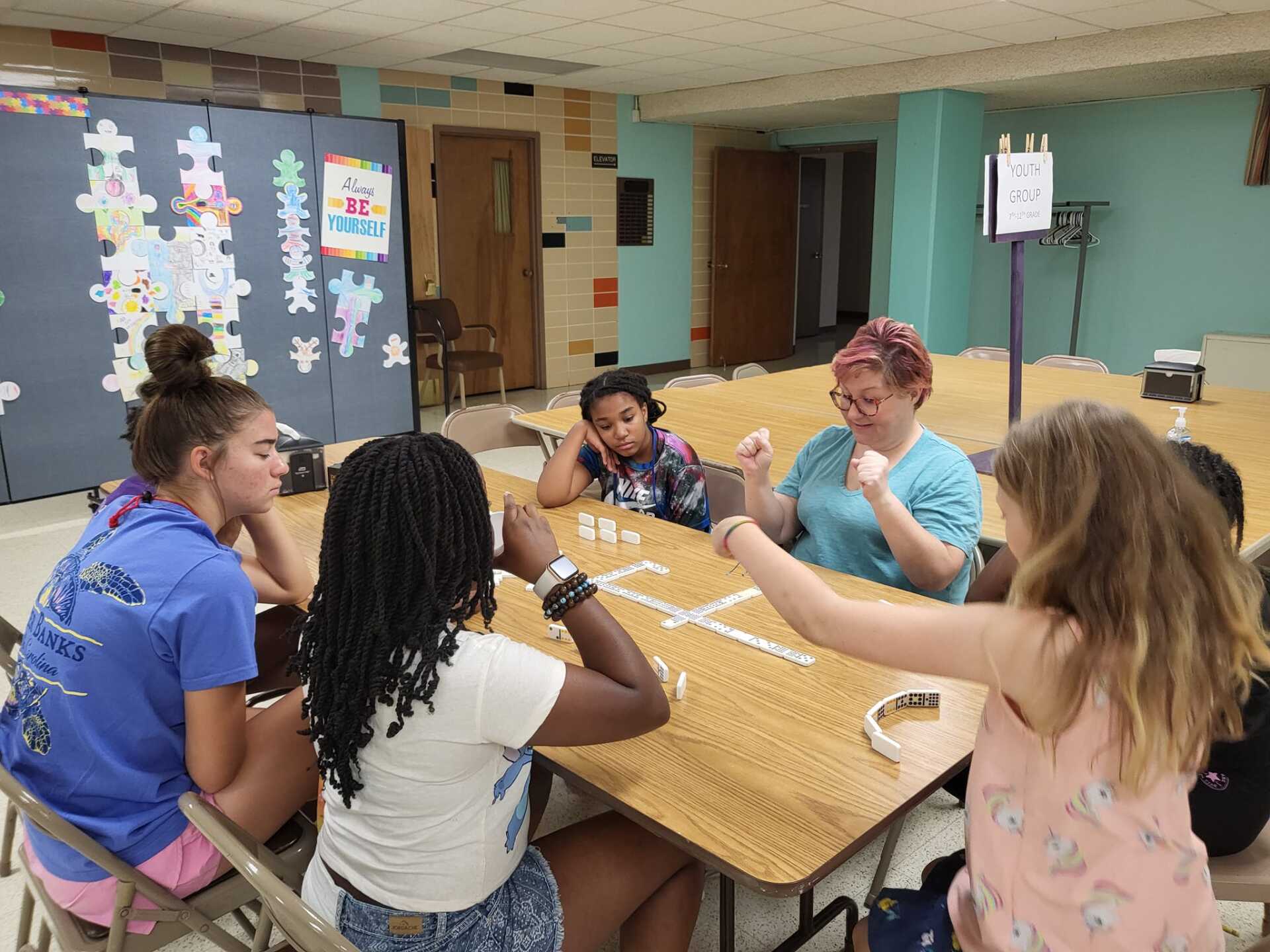 Group of people seated around a table in a community room, talking and gesturing during a meeting.