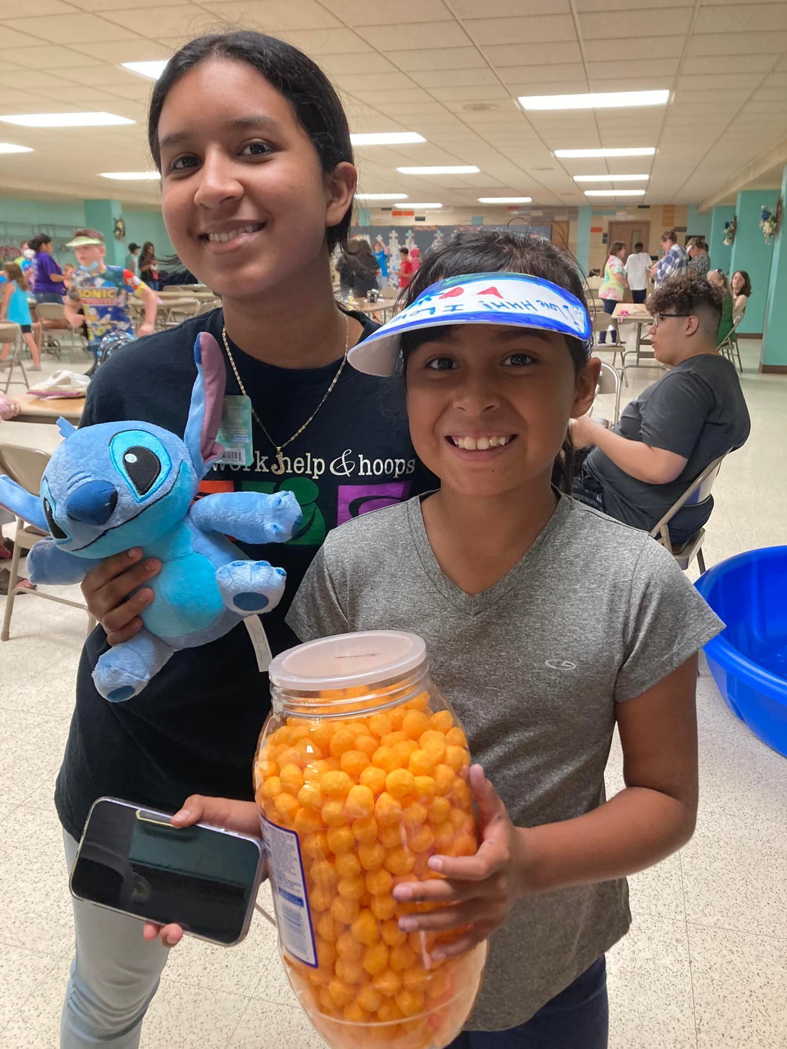 Two smiling children at a pool holding a blue plush toy and a jar of orange candy