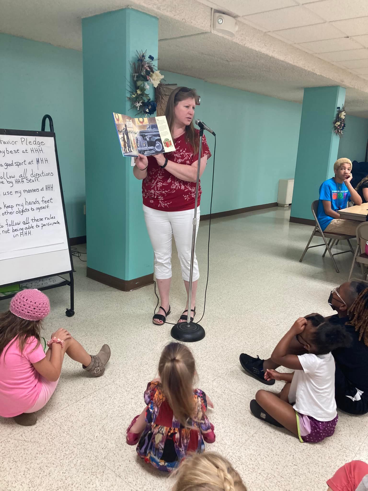 Woman presenting a poster to seated children in a teal community room