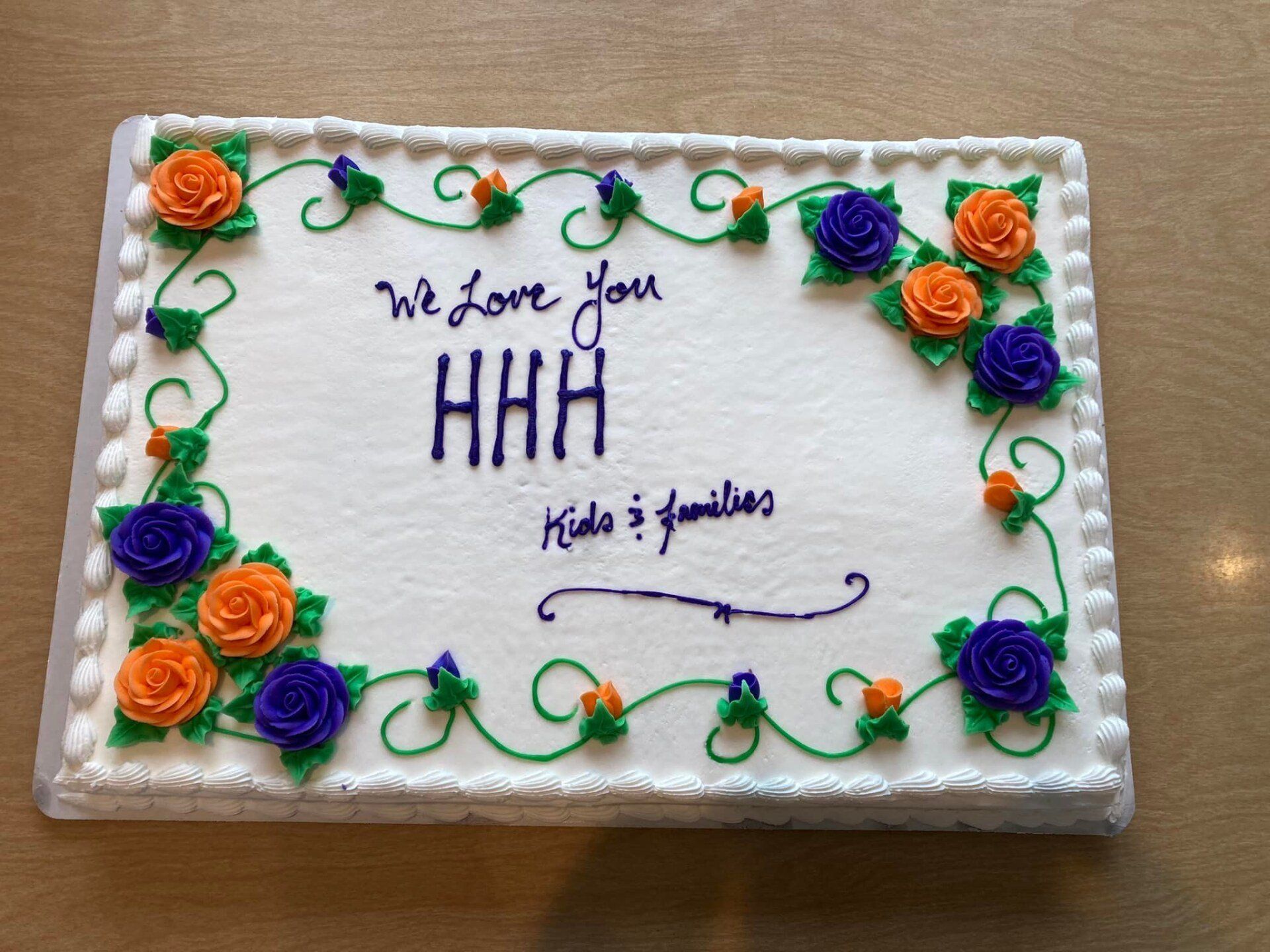Decorated white cake with orange and purple frosting flowers, “We love you HHH” and “Kids & grandkids” message