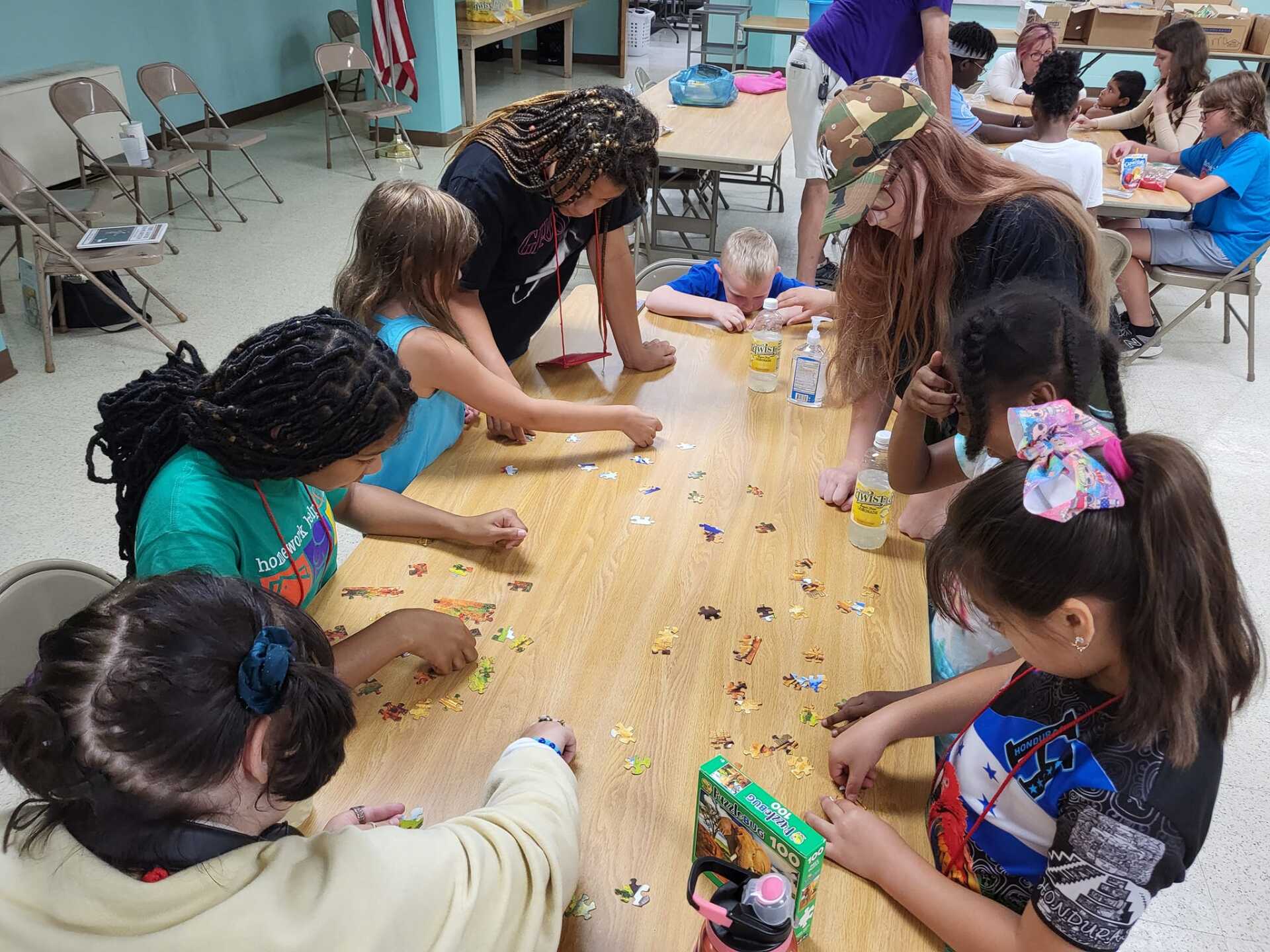 Children gather around a classroom table, leaning in and playing with small objects during an activity.