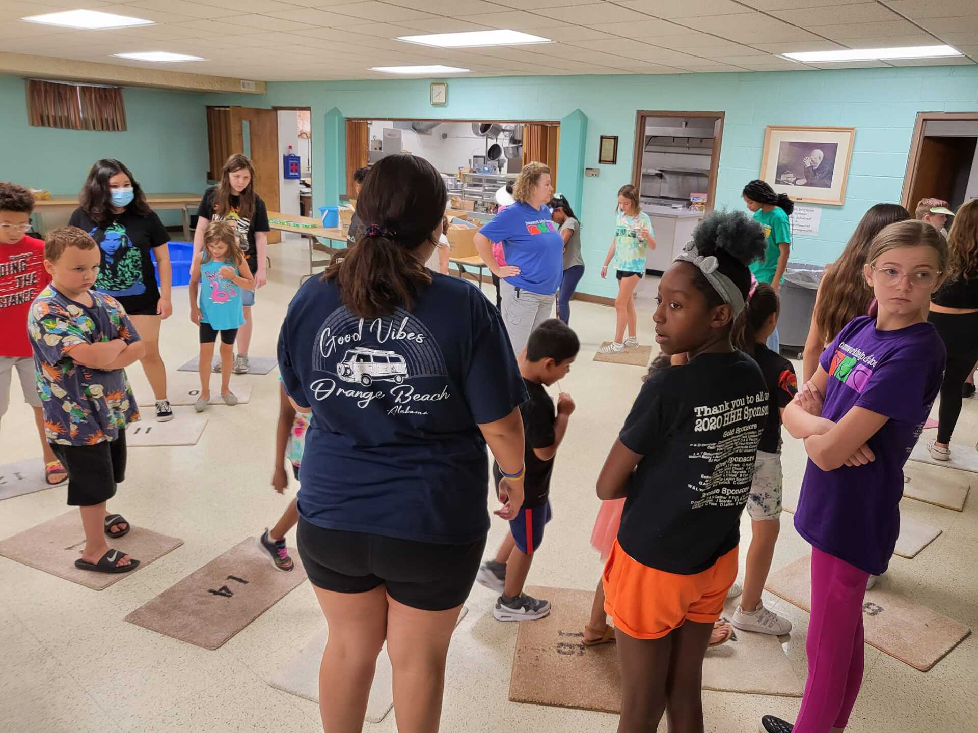Children in a gym stretch with an instructor, wearing colorful athletic clothes.