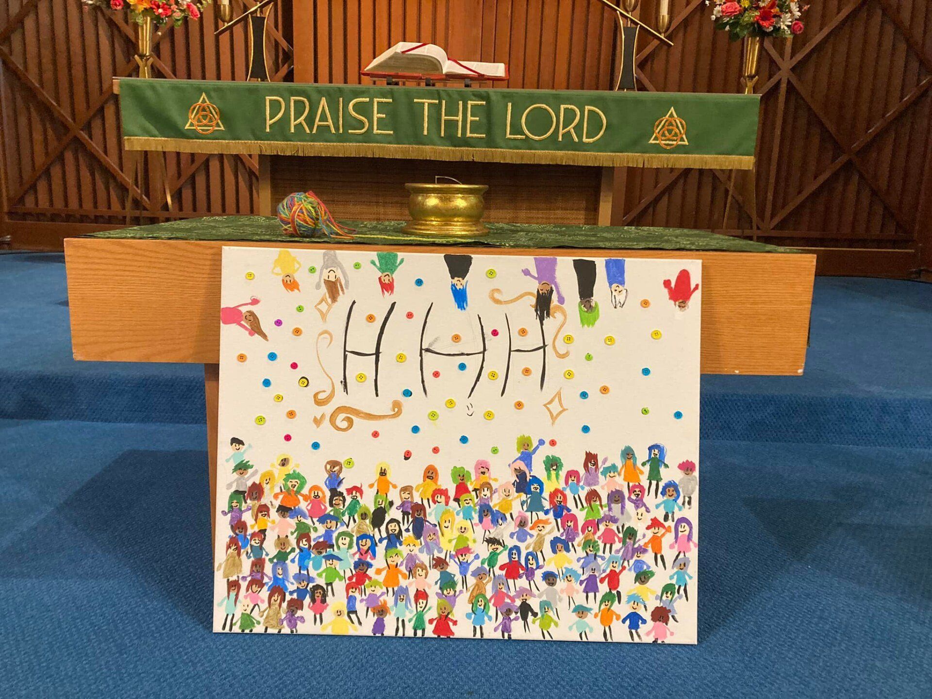 Children’s church artwork on an altar with “PRAISE THE LORD” banner and colorful crowd drawing