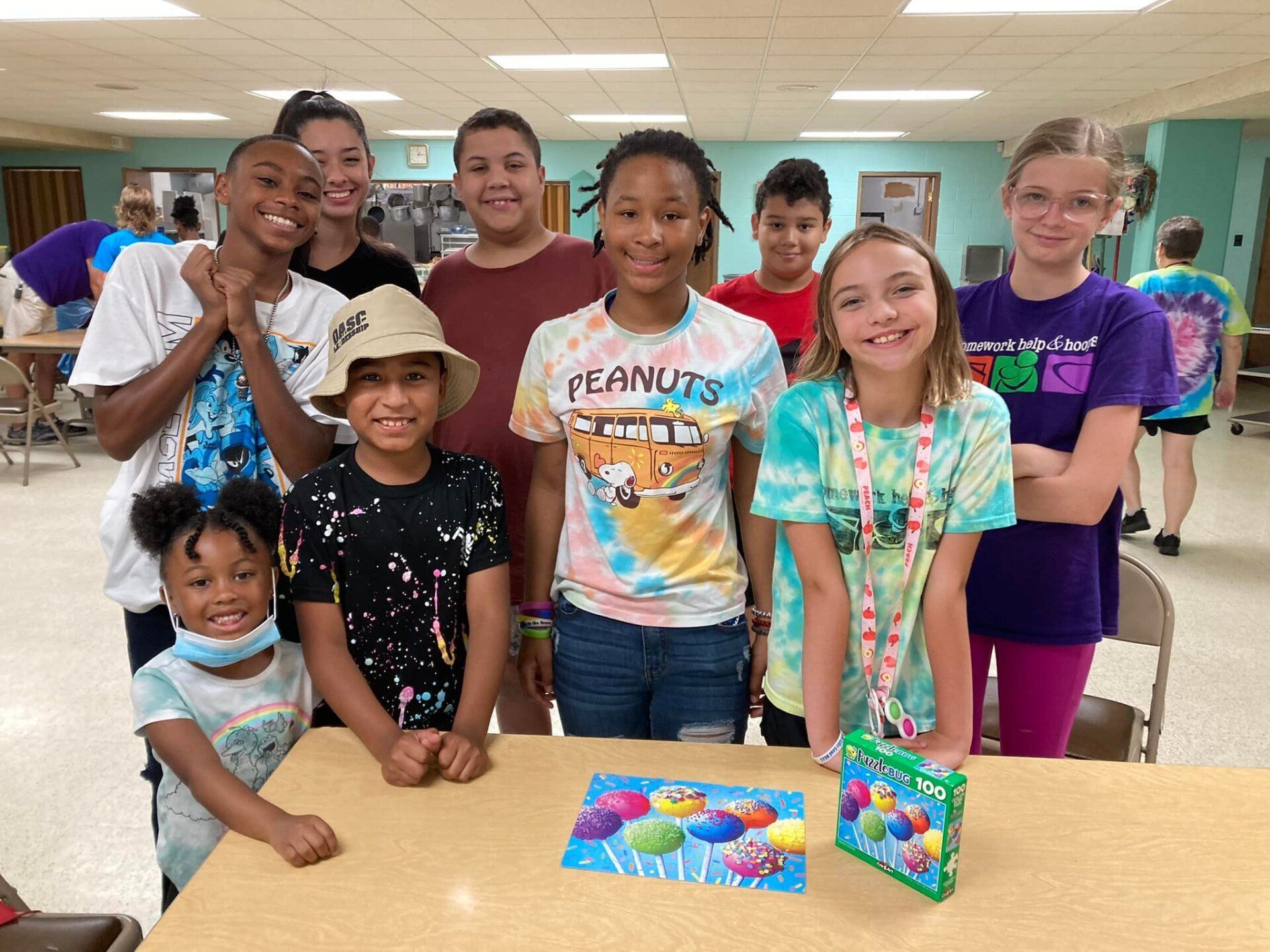 Group of smiling students posing in a classroom behind a table with colorful school supplies and books.