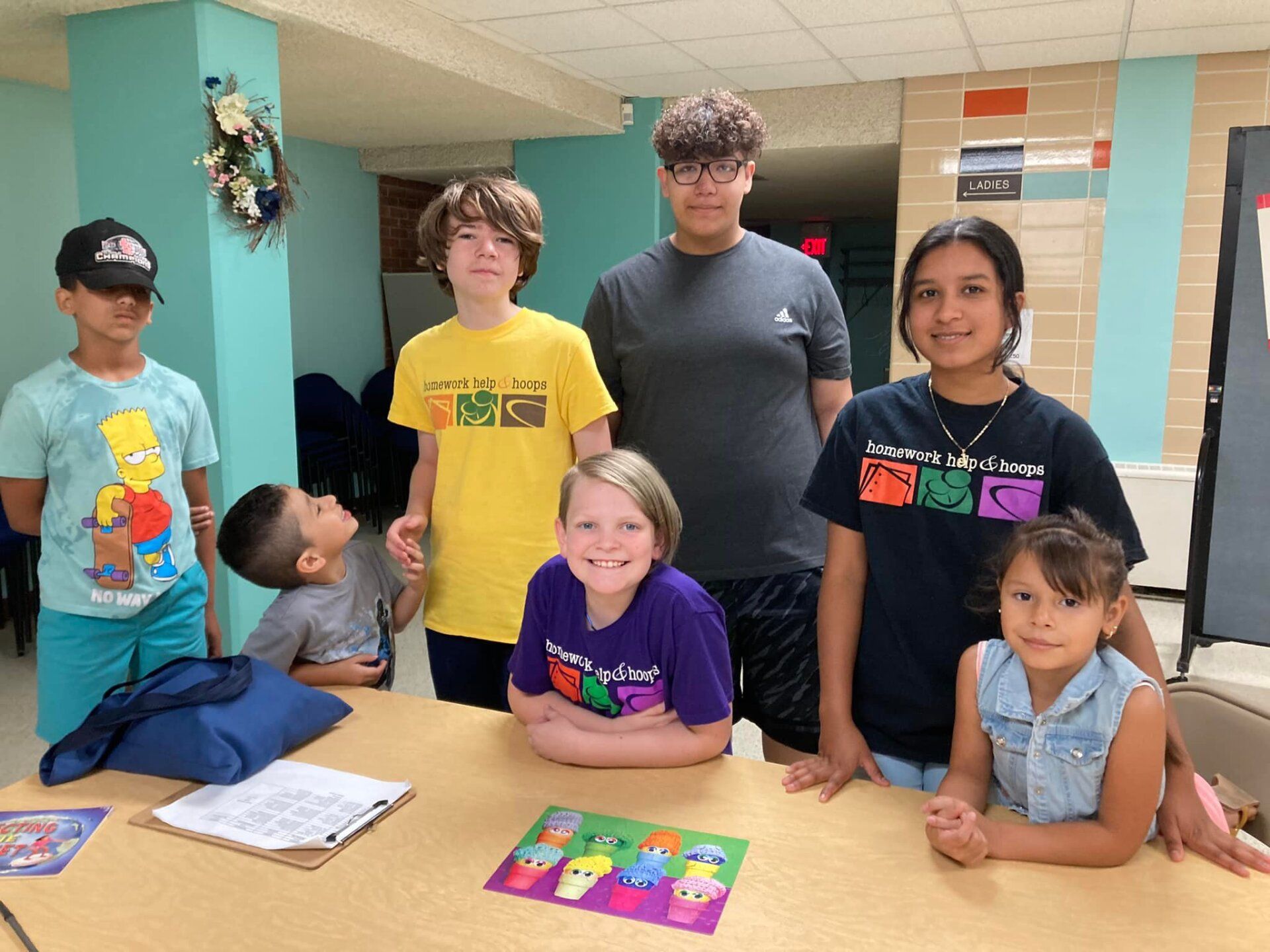 Children gathered around a table with colorful projects in a school hallway