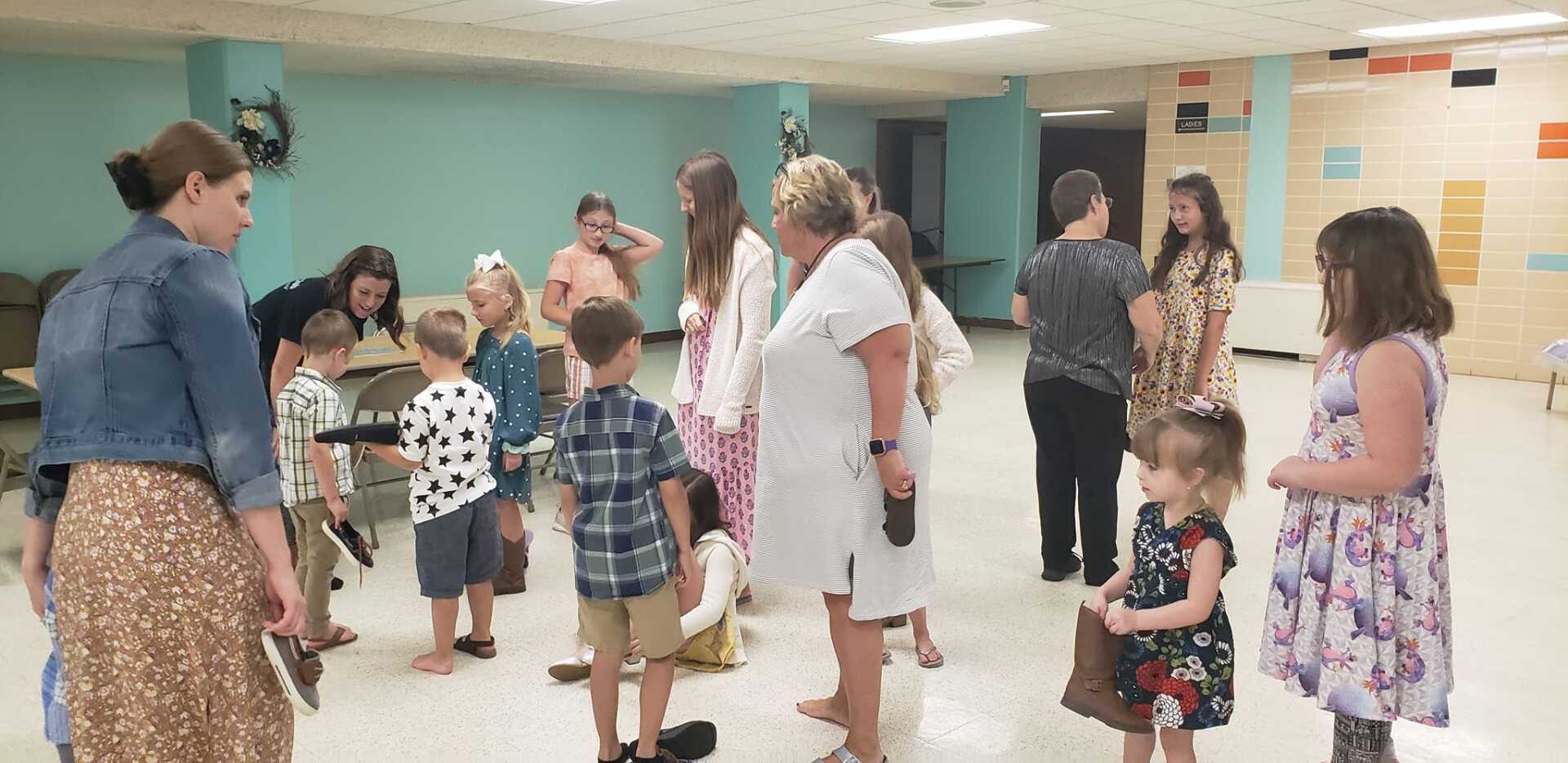 People mingling in a community hall, with adults and children chatting under teal walls and fluorescent lights