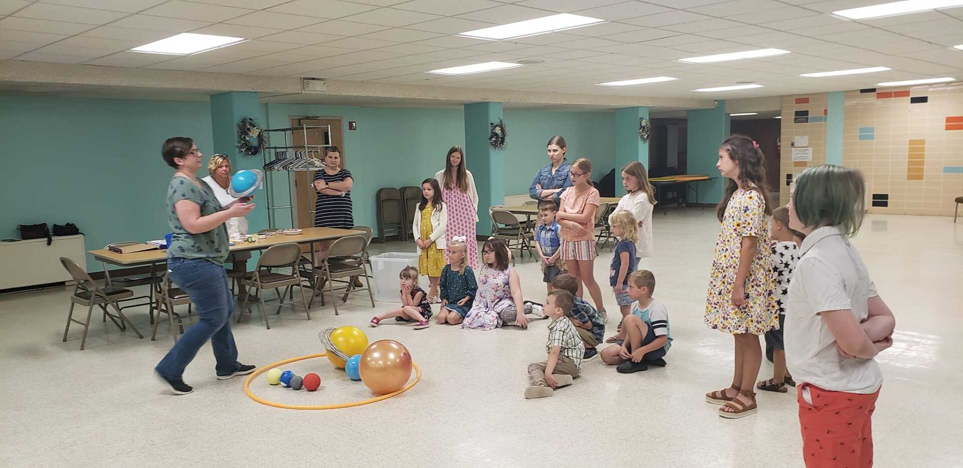 People gathered in a community room, some standing and some seated around toys on the floor.