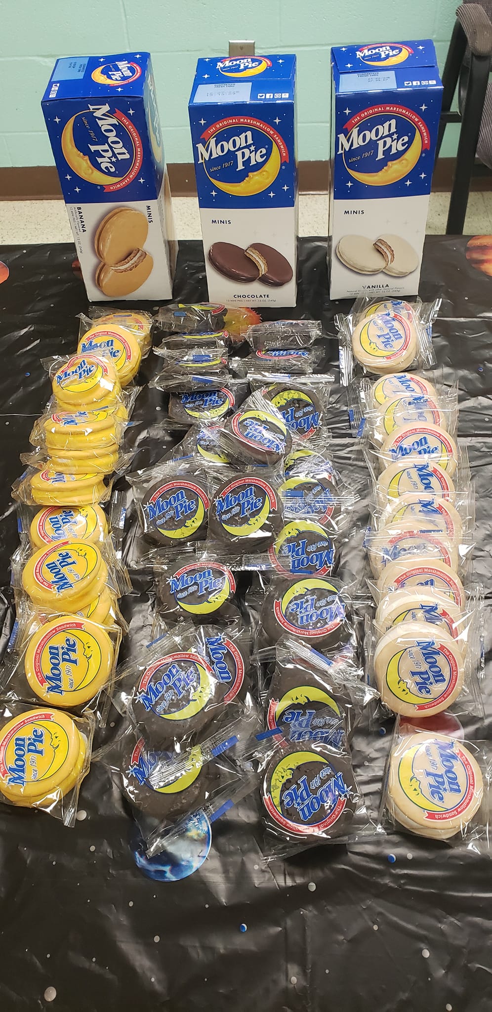 Assorted snack packages and boxes arranged in rows on a black tablecloth.