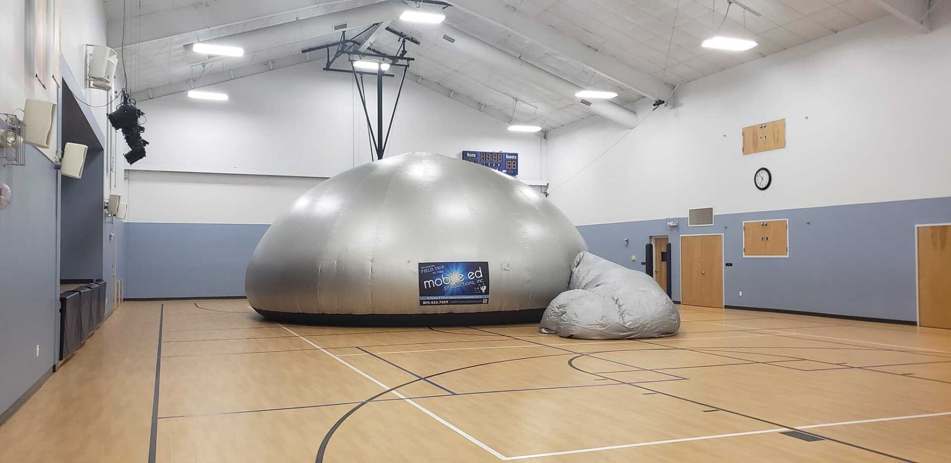 Indoor gym with a large silver dome structure and a gray padded mound under bright ceiling lights.