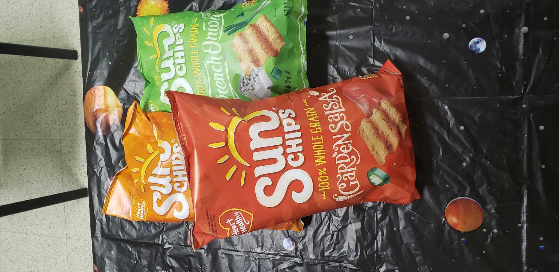 Three snack packets on a black surface, including red and green chips bags.