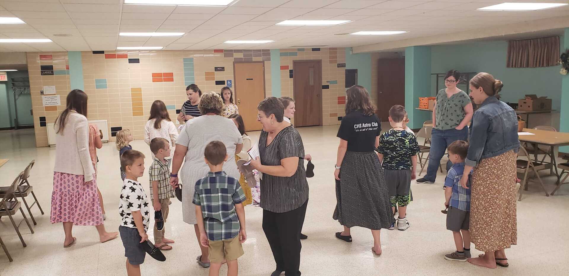 People socializing in a community room with tiled floor, folding chairs, and a chalkboard on the wall.