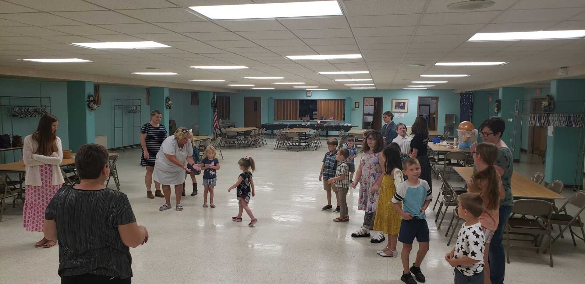 People dancing in a large community hall with bright turquoise walls and rows of tables along the back.