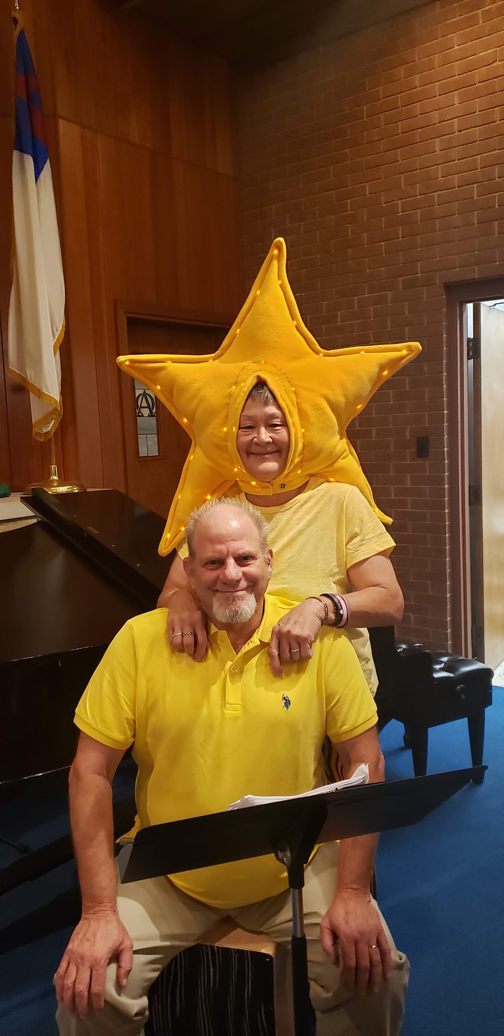Two people in yellow costumes pose indoors, one wearing a large star-shaped headpiece.